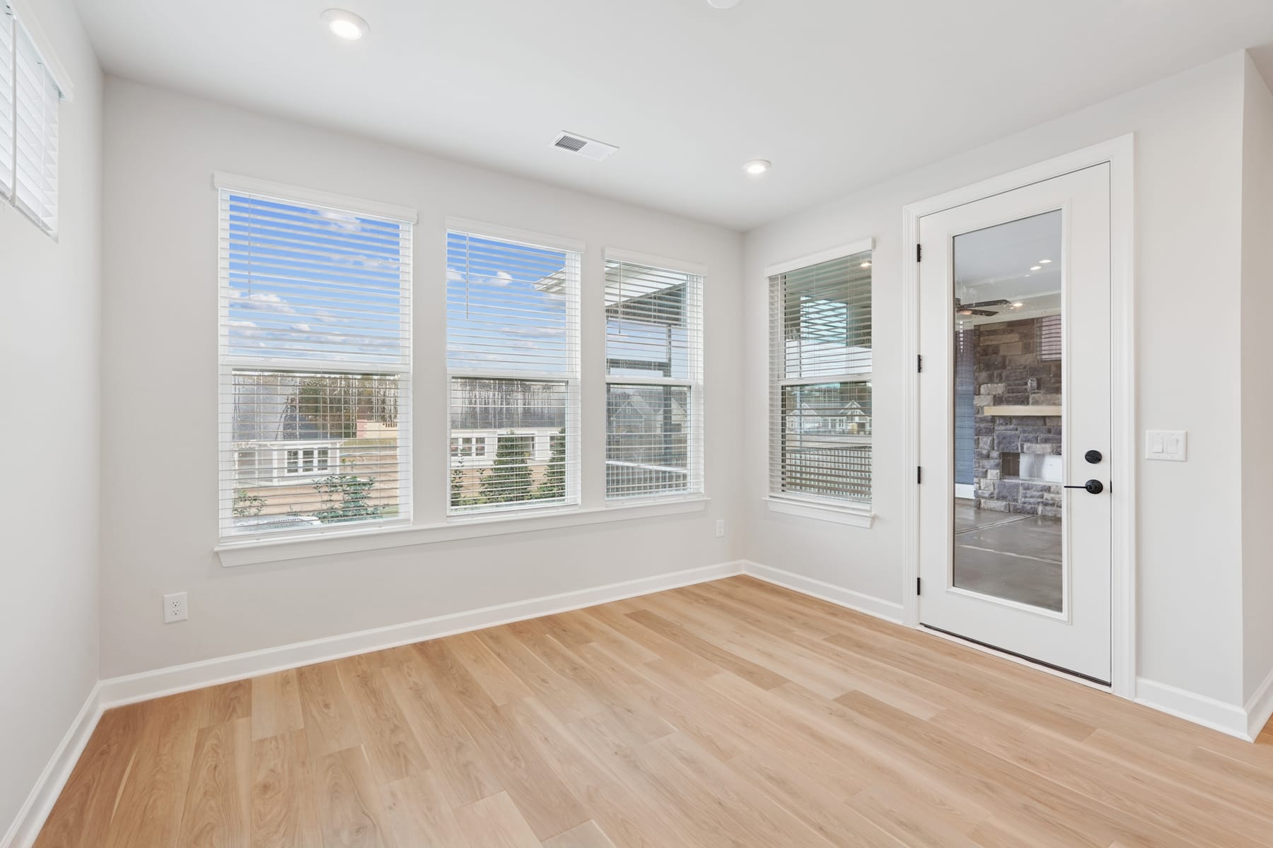 A bright and airy room with large windows, hardwood floors, and a white door leading to another area.