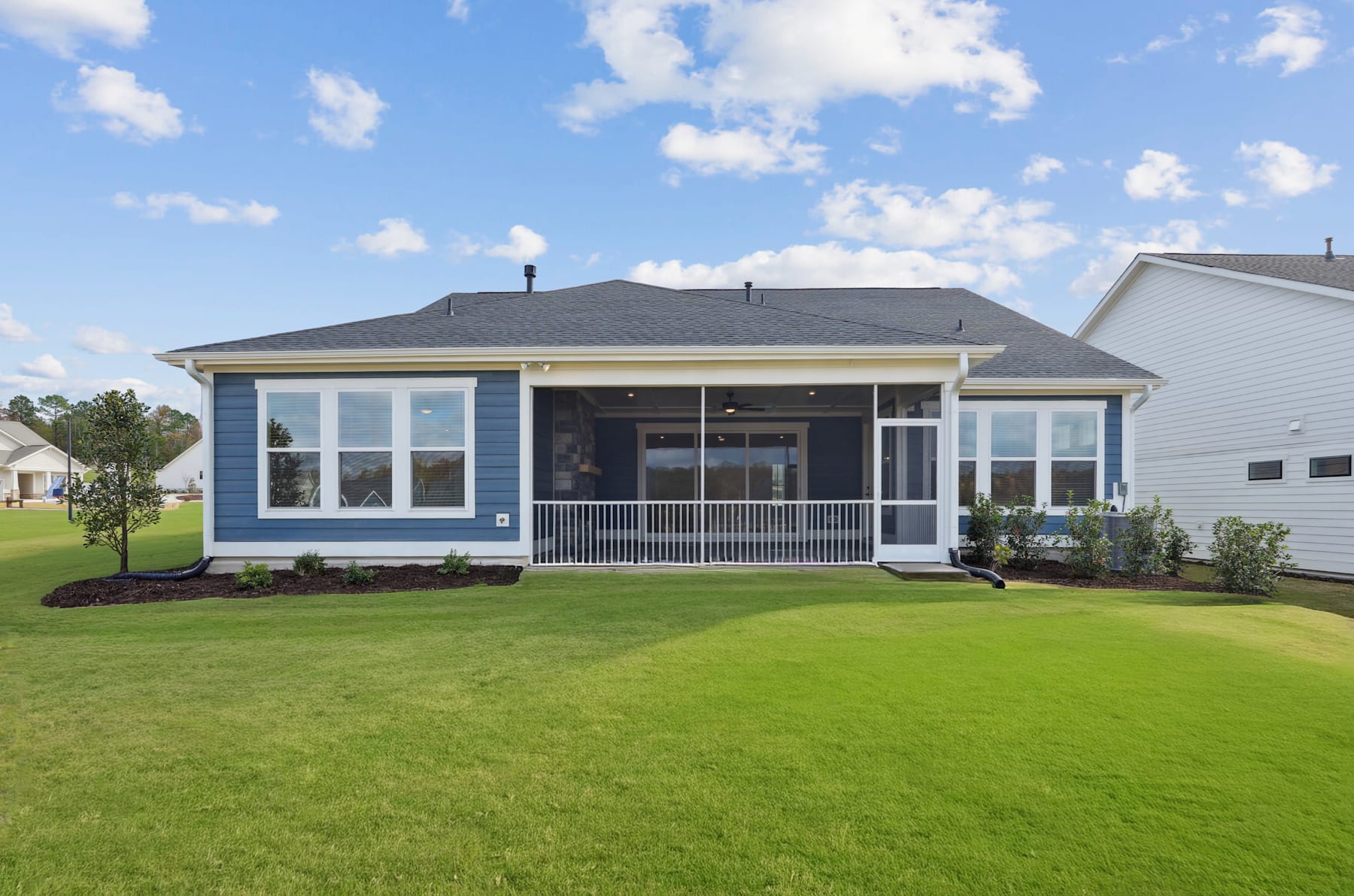 A single-story house with a porch, surrounded by a well-manicured lawn and set against a blue sky with fluffy white clouds.