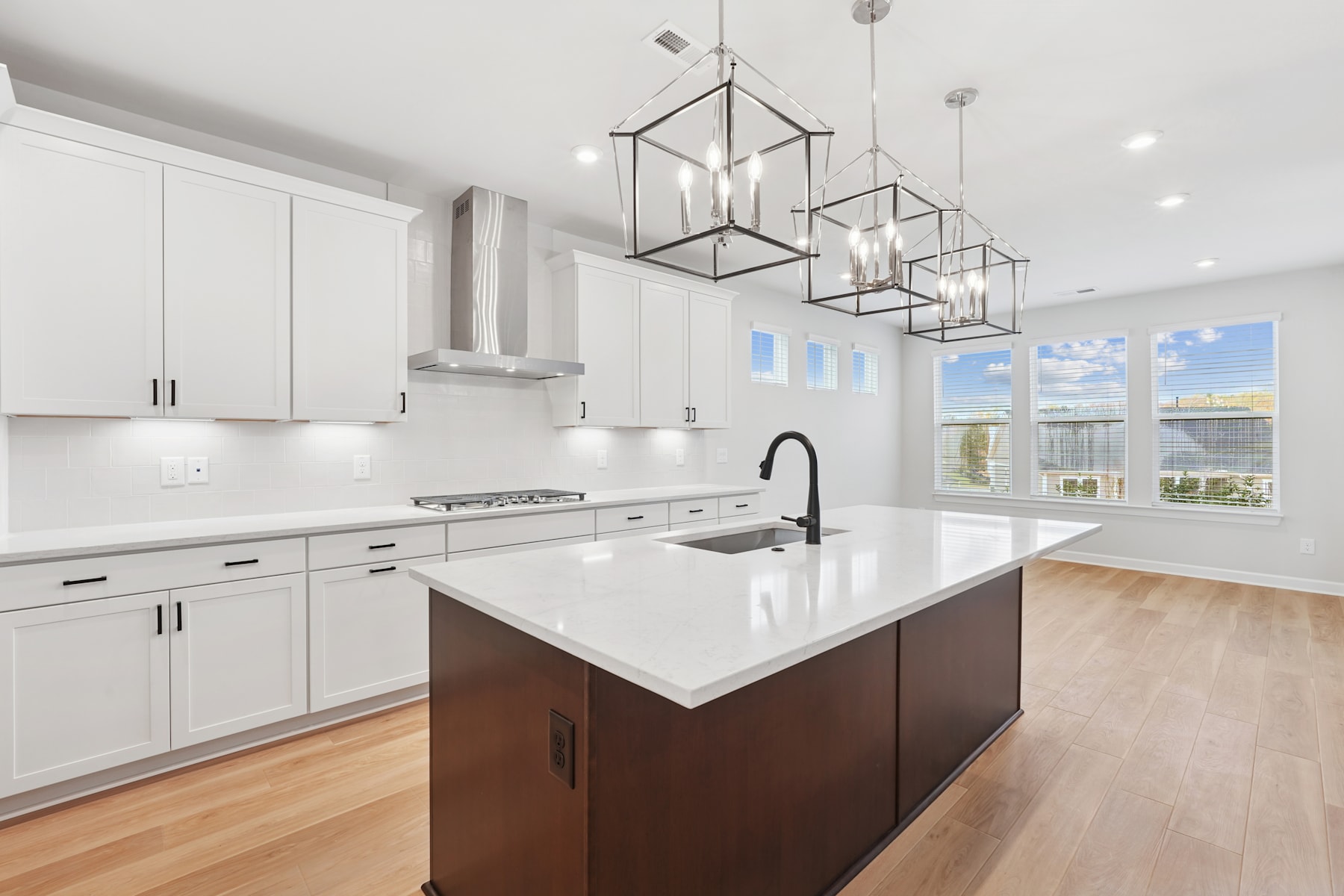 A modern, open-concept kitchen with white cabinets, a large island with a white countertop, and pendant lighting fixtures hanging above.