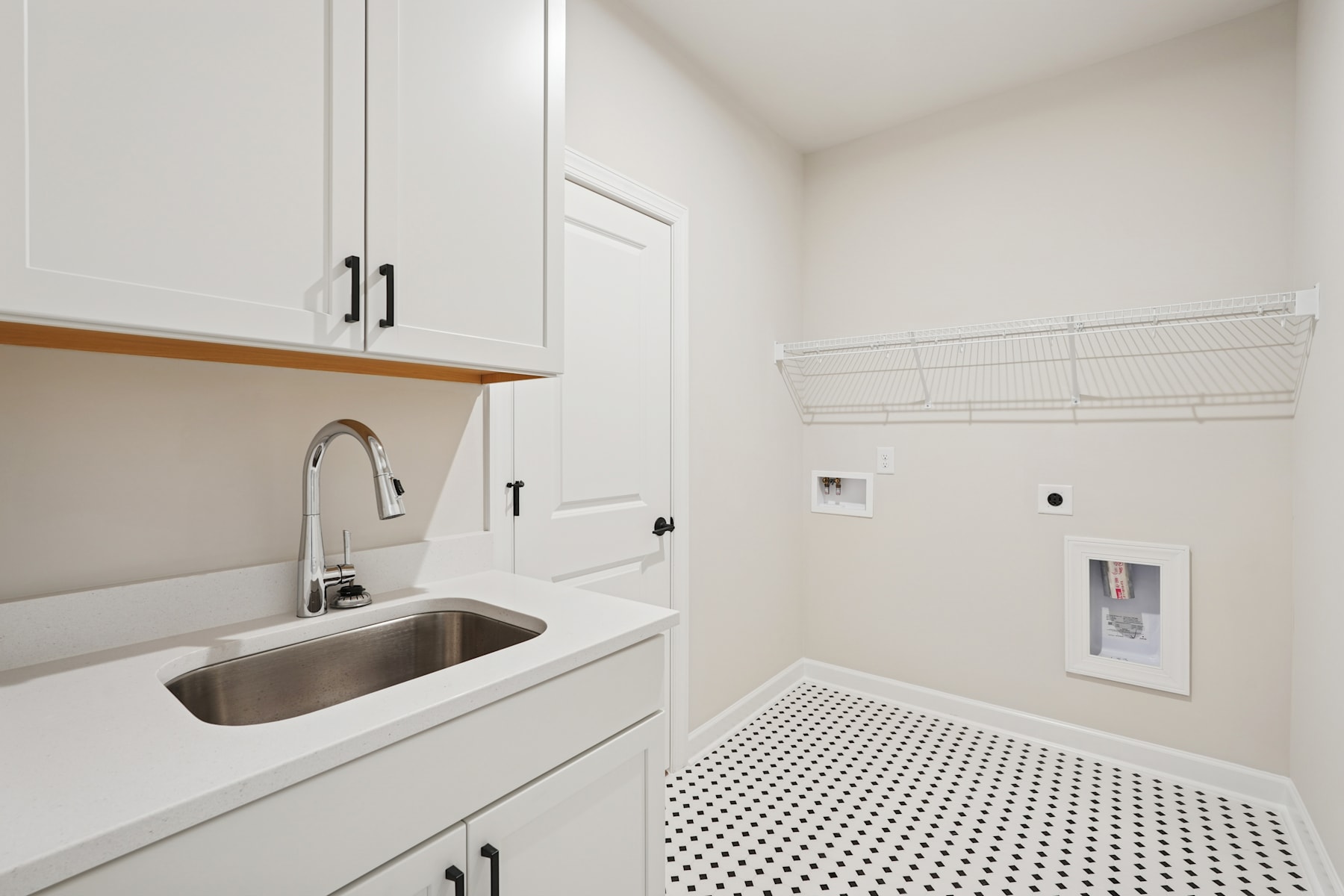 A modern, minimalist laundry room with white cabinets, a stainless steel sink, and a tiled floor with a polka dot pattern.