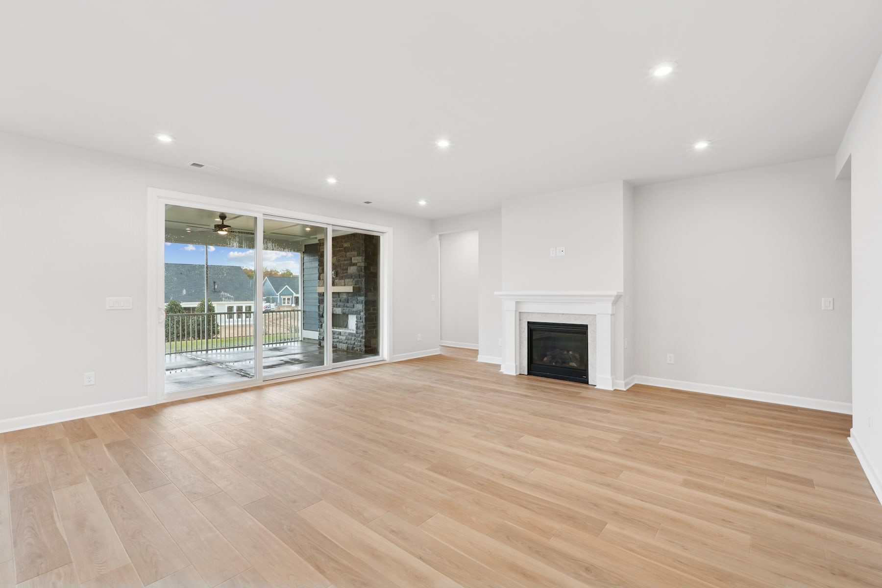 A spacious, well-lit room with a fireplace and large windows overlooking a scenic outdoor area, featuring hardwood floors and a minimalist, modern design.