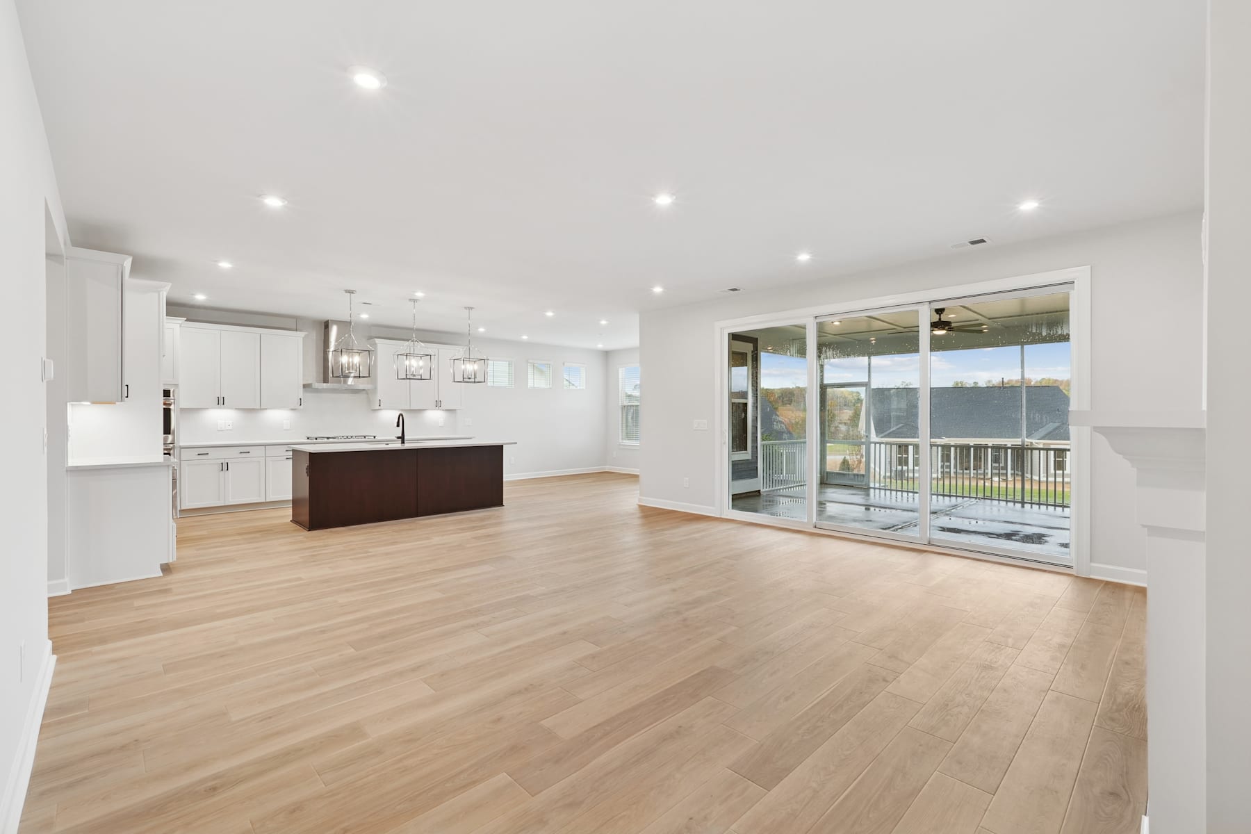 A modern, open-concept kitchen and living room with white walls, hardwood floors, and large windows providing ample natural light.
