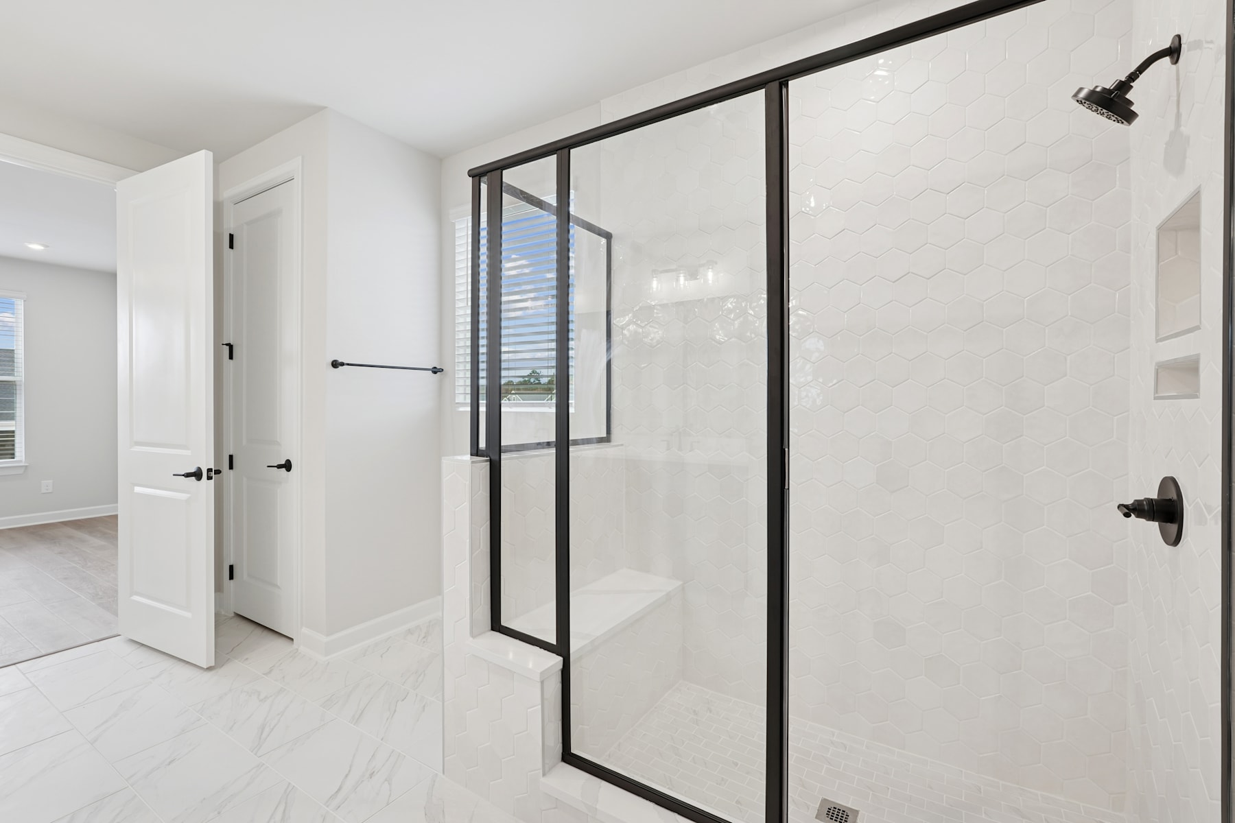 A modern, minimalist bathroom with a large glass shower enclosure, white walls, and a black metal frame.
