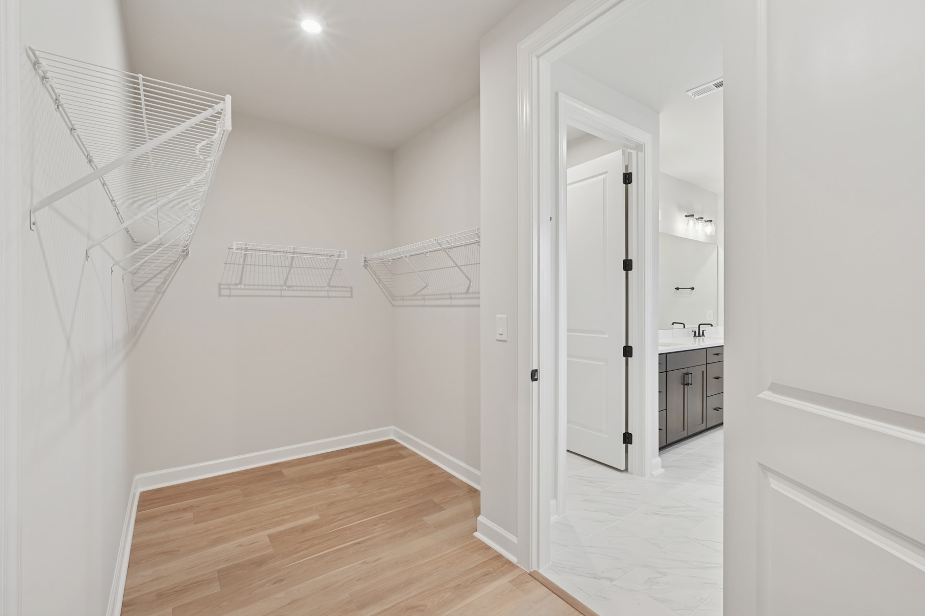 A bright, minimalist hallway with white walls, wooden flooring, and a closet with wire shelving visible in the background.
