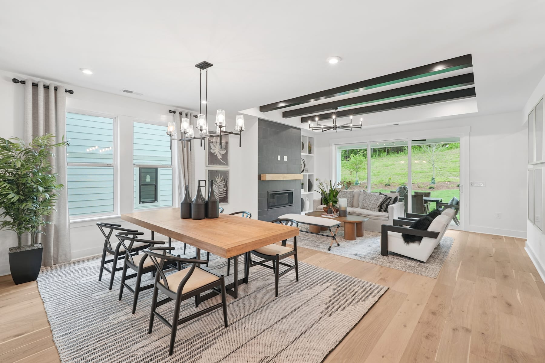 A modern and open-concept living space with a dining area, comfortable seating, and large windows overlooking a lush outdoor environment.