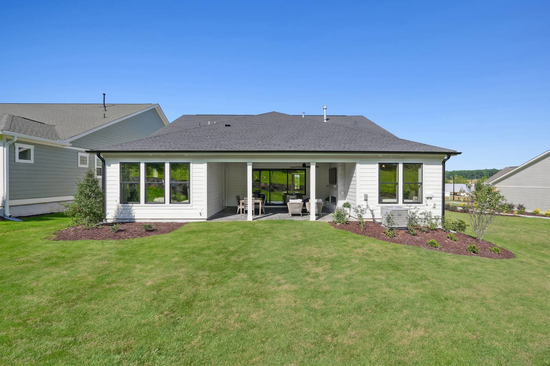 A well-manicured lawn surrounds a modern, single-story house with a covered porch and large windows, set against a clear blue sky.