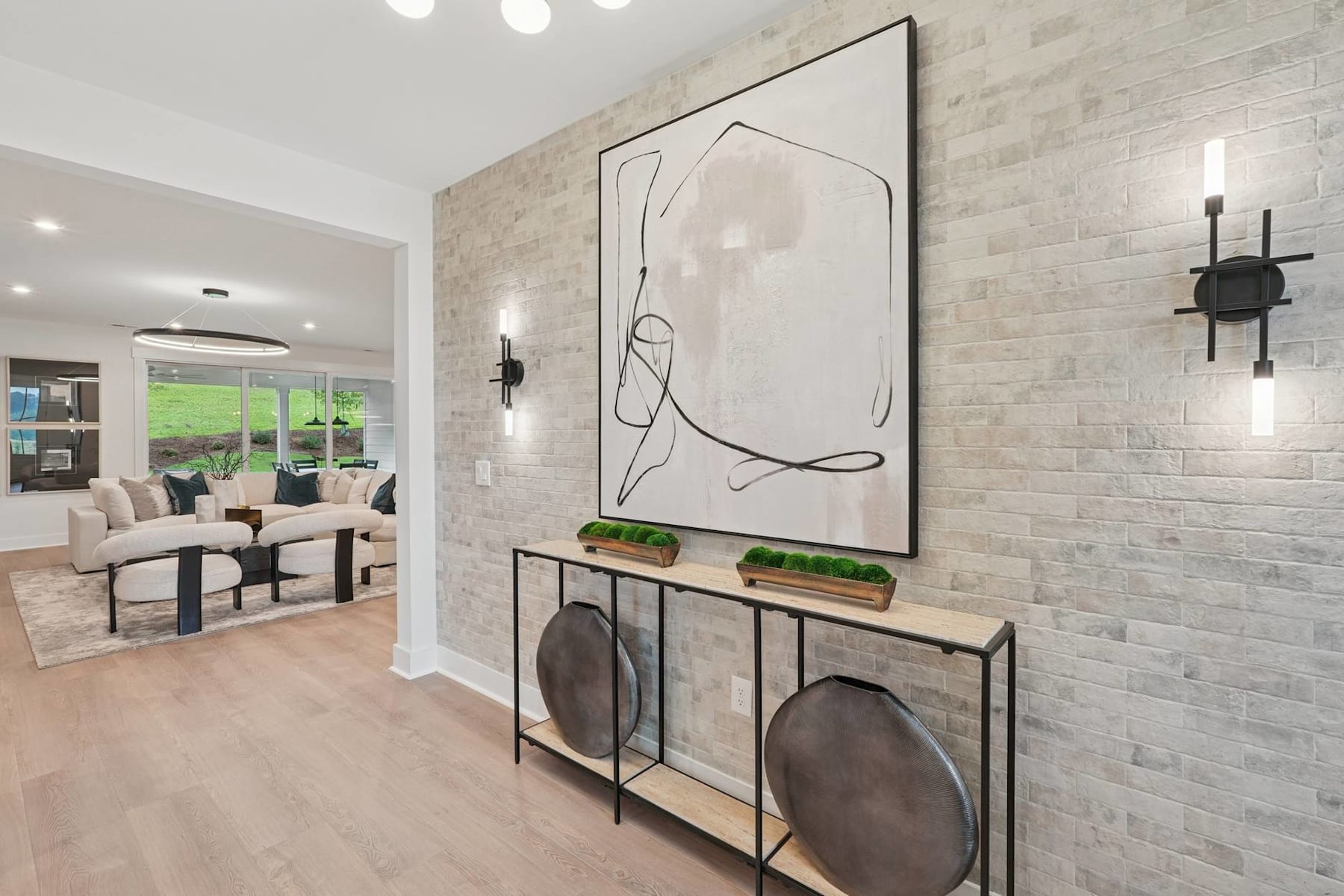 A modern and minimalist entryway with a large abstract artwork, a wooden console table, and a brick wall backdrop, creating a stylish and inviting atmosphere.