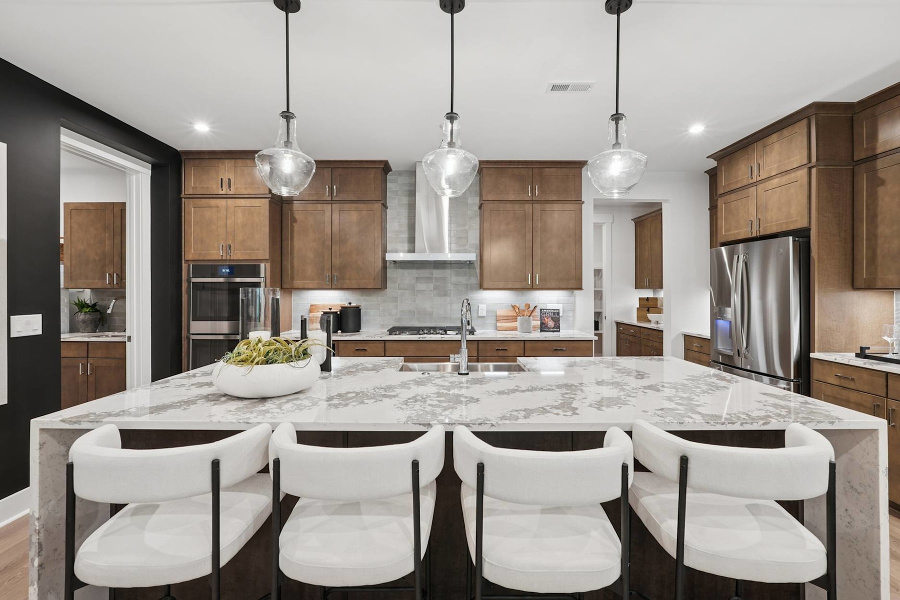 A modern and spacious kitchen with a large marble-topped island, wooden cabinets, and pendant lighting fixtures, creating a stylish and functional living space.