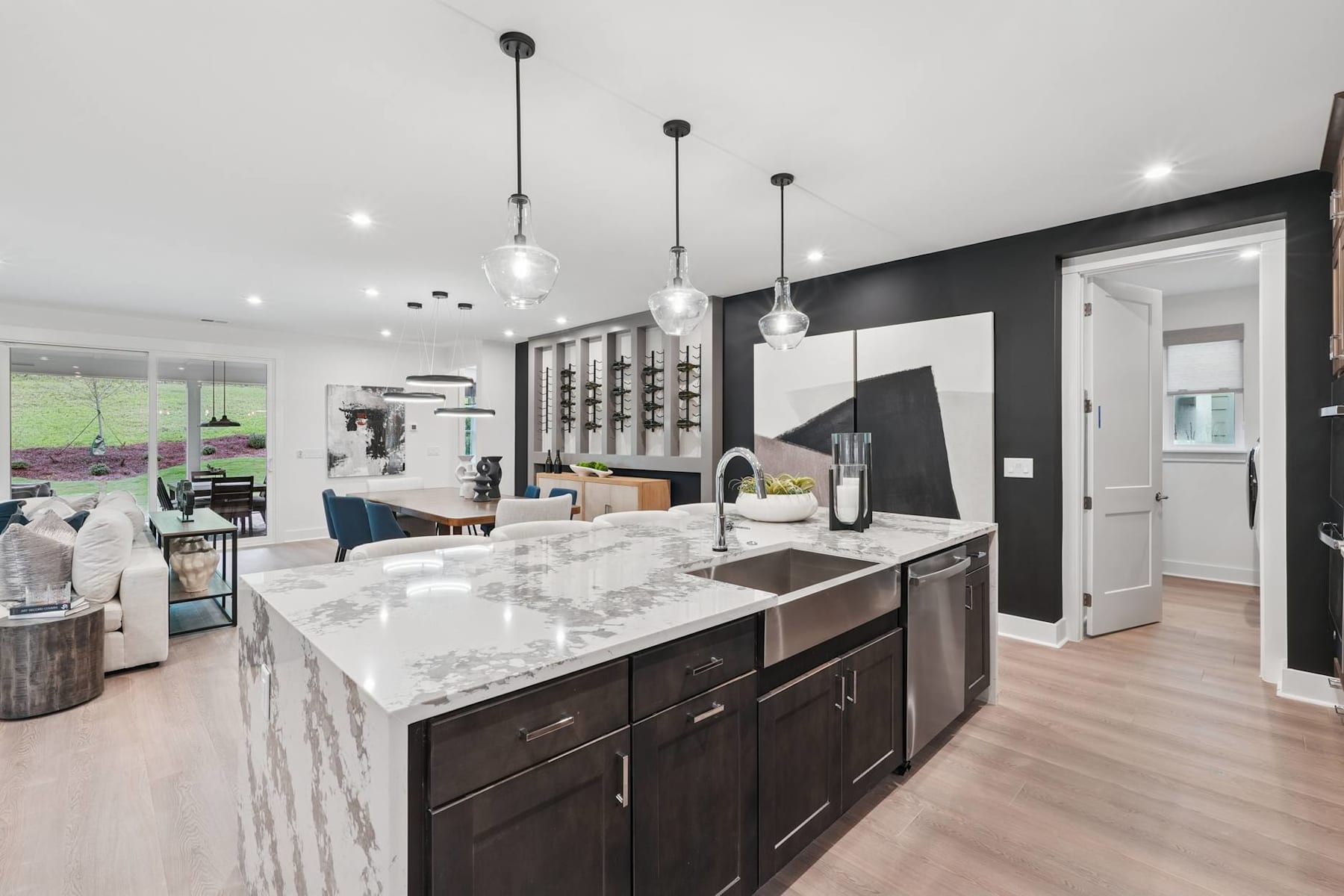 A modern and stylish kitchen with a large marble-topped island, dark cabinets, and pendant lighting fixtures, set against a bright and airy background.