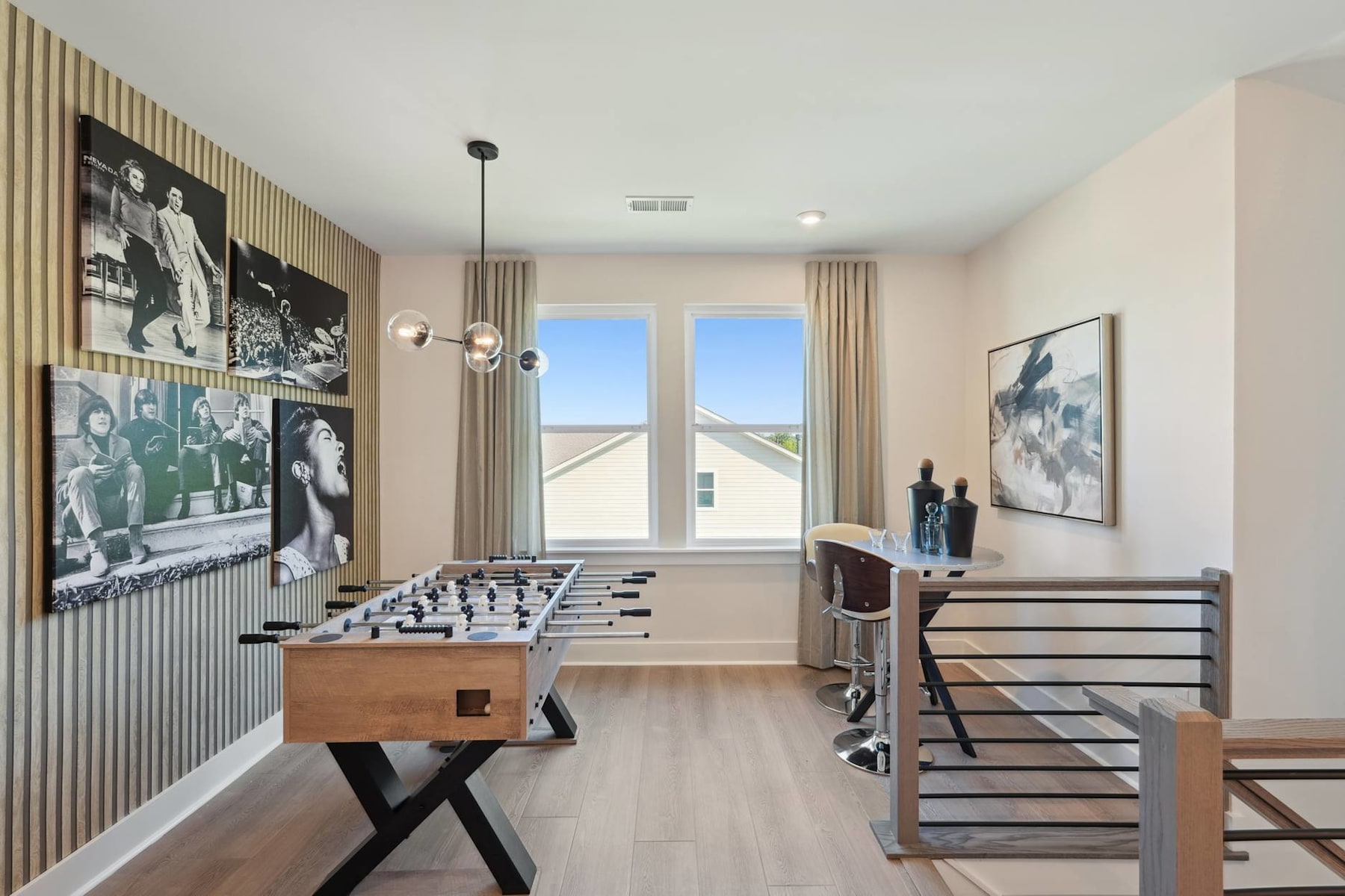 A modern and minimalist game room with a foosball table, artwork on the walls, and large windows providing natural light.