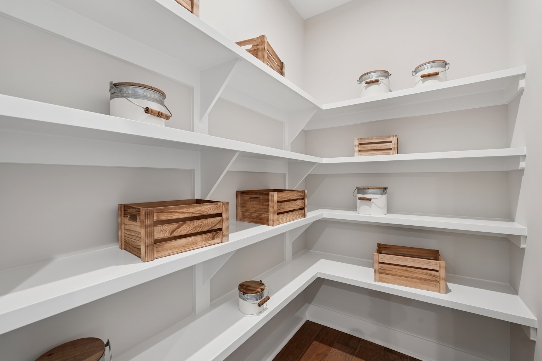 A well-organized pantry with white shelves and wooden crates, creating a clean and minimalist storage space.