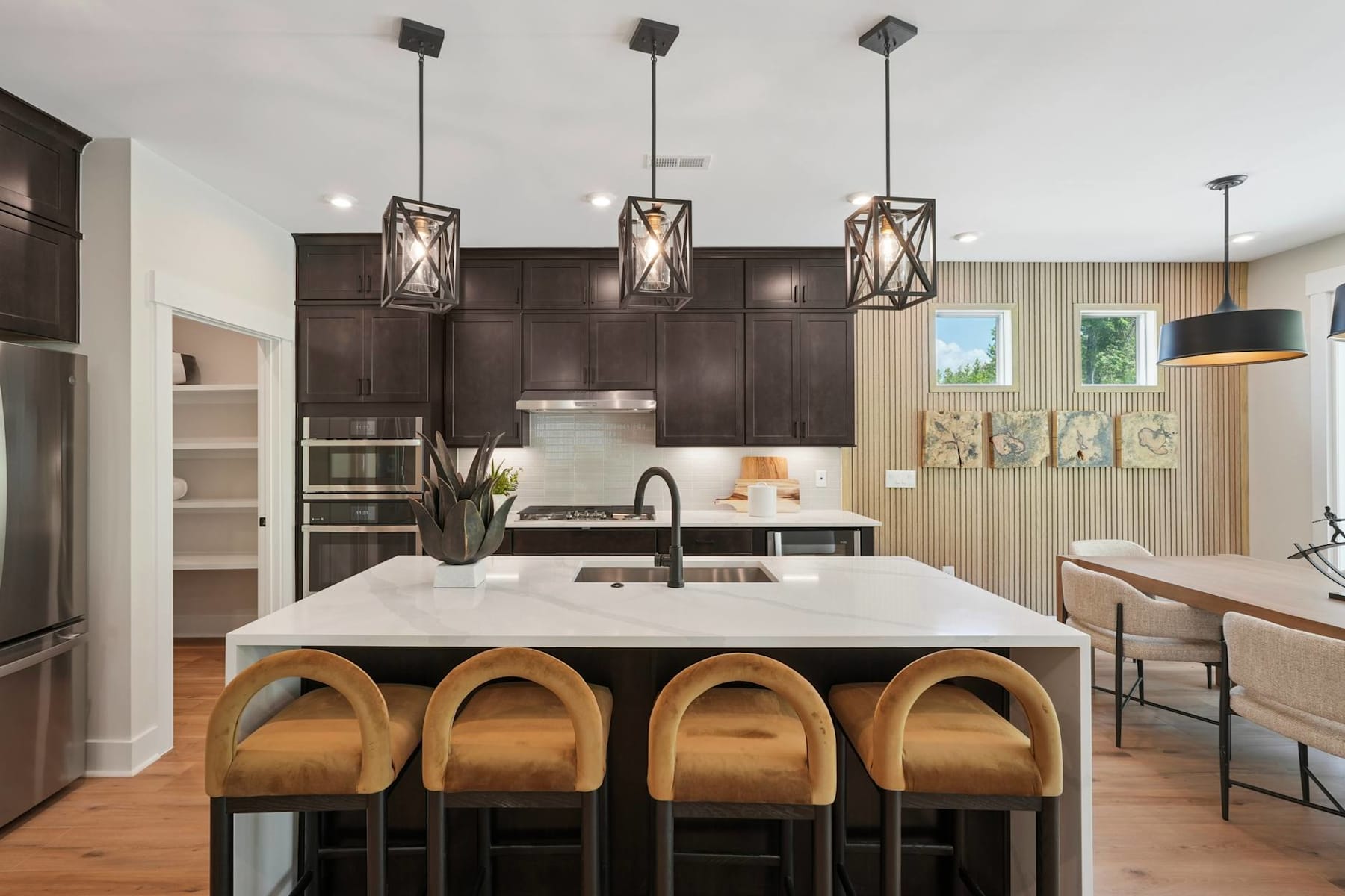 A modern kitchen with dark cabinets, a white countertop, and pendant lights above a central island with wooden stools.