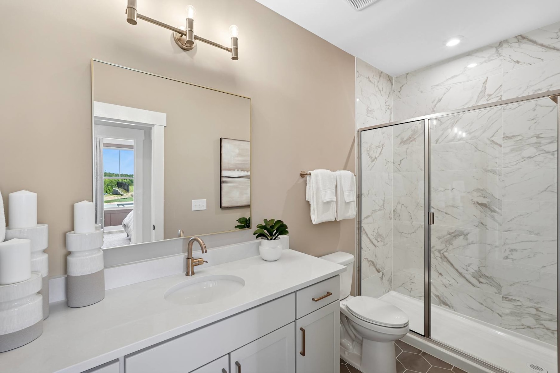A modern and spacious bathroom with a marble-like vanity, a glass shower enclosure, and a large window providing natural light.