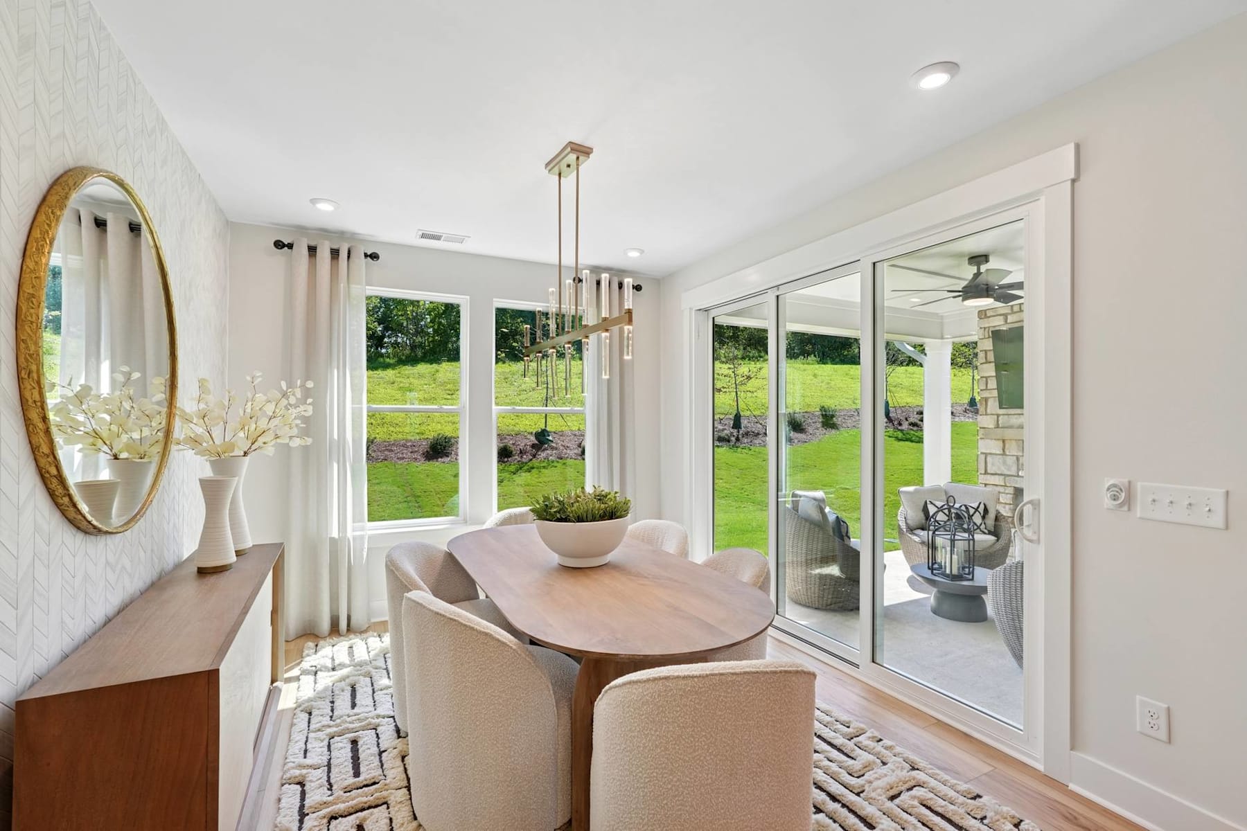 A bright and airy dining room with a wooden table and chairs, surrounded by large windows overlooking a lush green outdoor space.