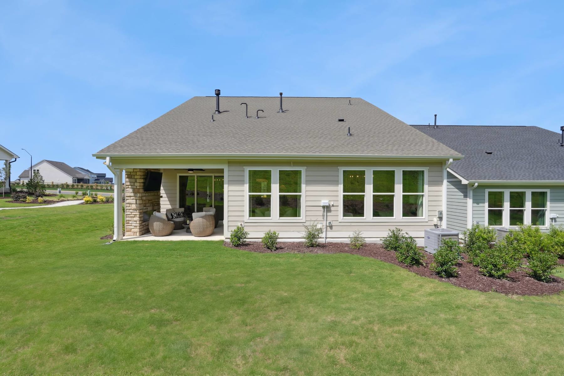 A well-maintained suburban home with a lush green lawn in the foreground, surrounded by a neatly landscaped yard and a clear blue sky in the background.