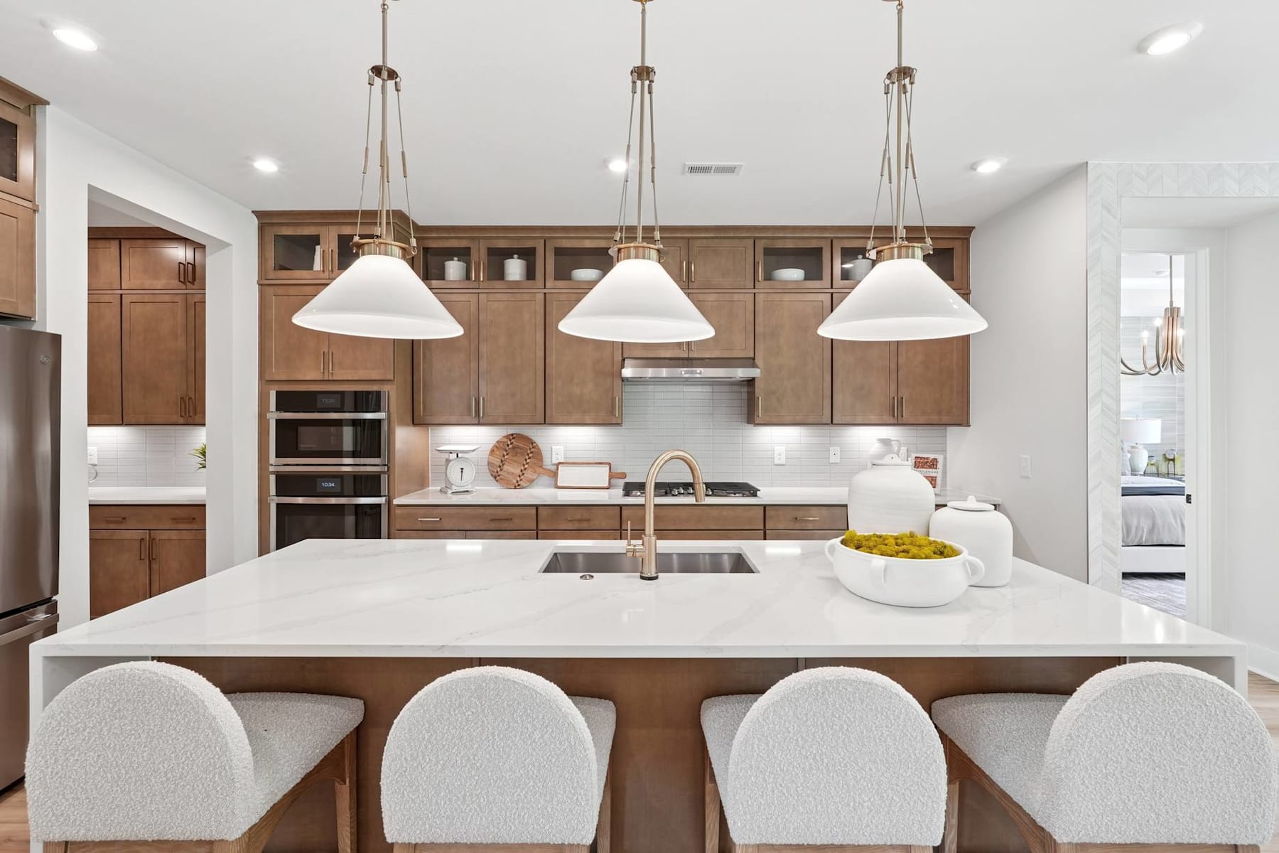 A modern, well-lit kitchen with wooden cabinets, a large white island, and pendant lights hanging above.