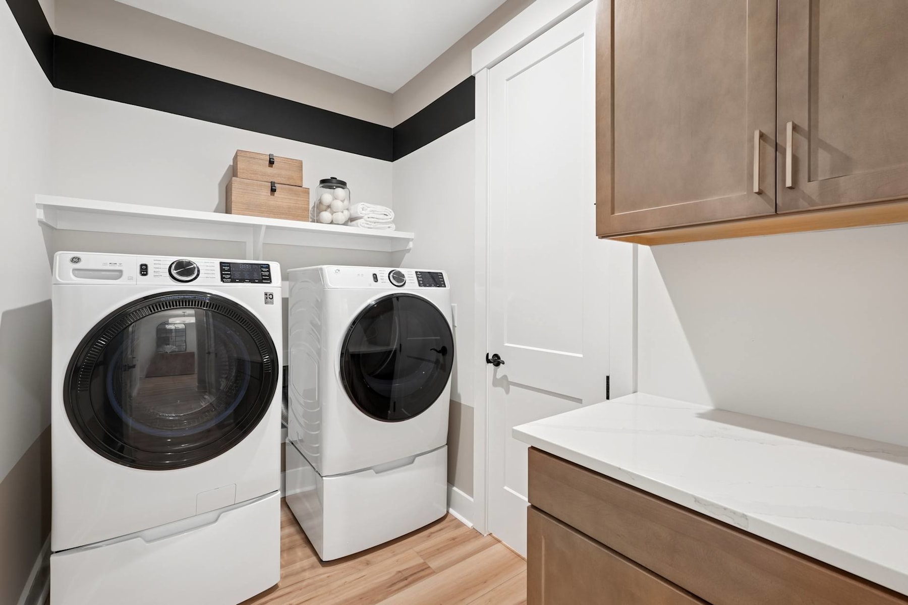 A modern and well-organized laundry room with a white washer and dryer, wooden cabinets, and a white countertop.