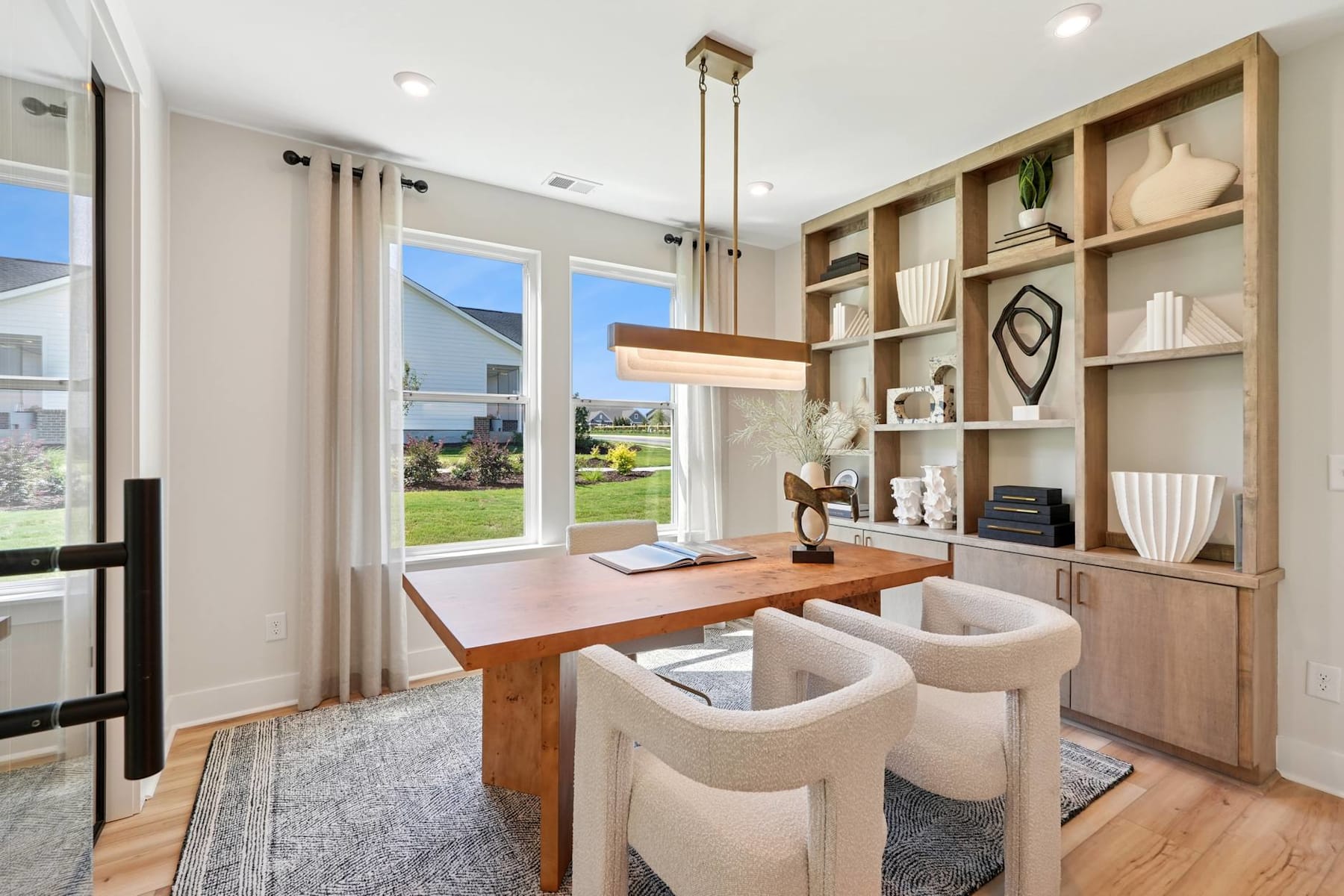 A modern and cozy home office space with a wooden desk, built-in shelves, and comfortable seating, surrounded by large windows overlooking a scenic outdoor landscape.