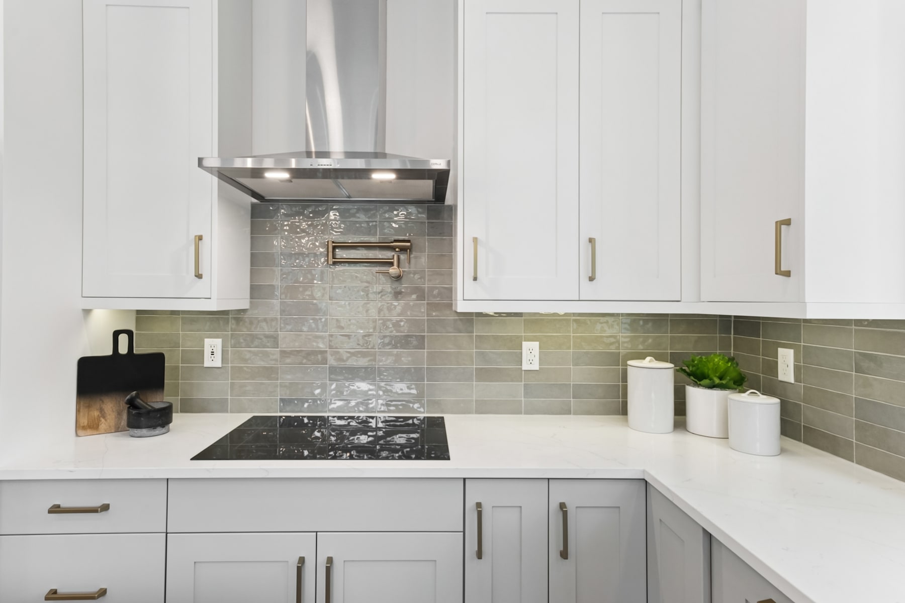 A modern, well-designed kitchen with white cabinets, gray countertops, and a tile backsplash, featuring a stainless steel range hood and appliances.