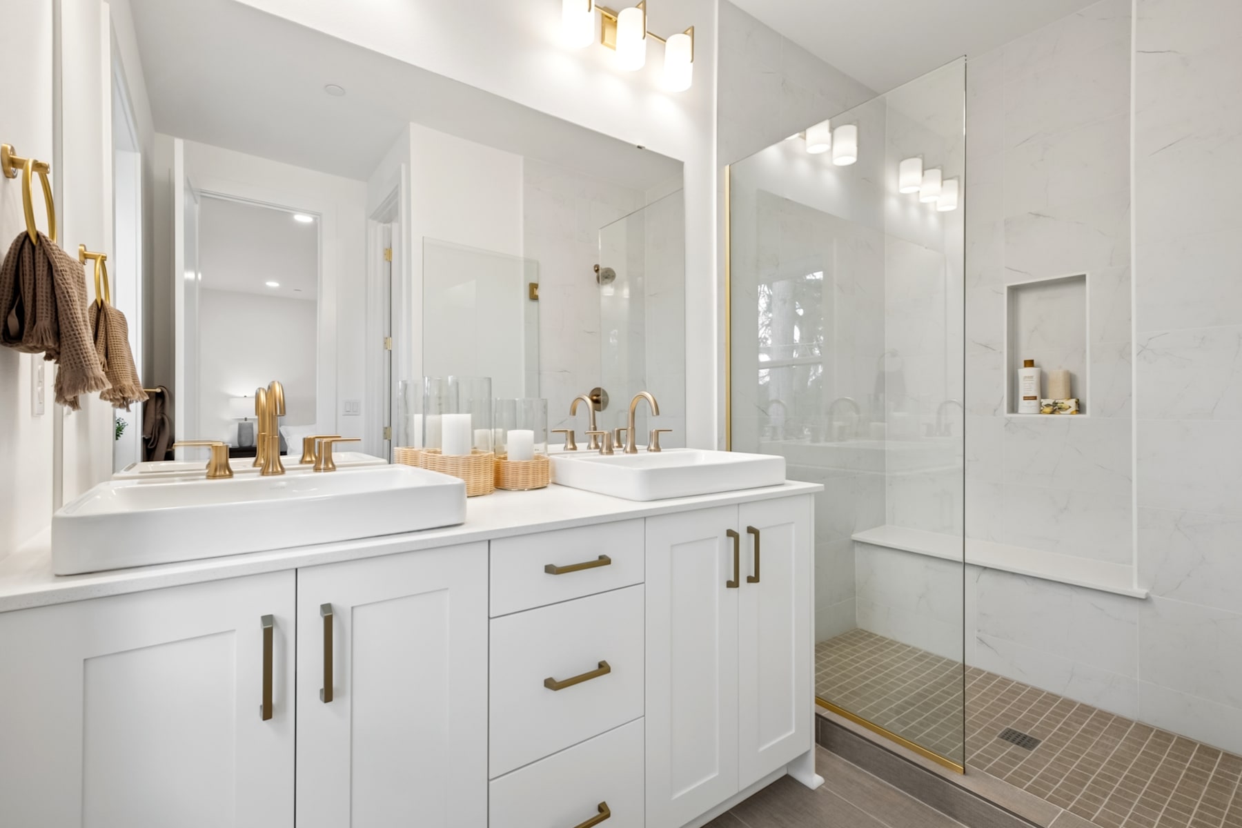 A modern, well-lit bathroom with a white vanity, a vessel sink, and brass fixtures, surrounded by white walls and a tiled shower area.