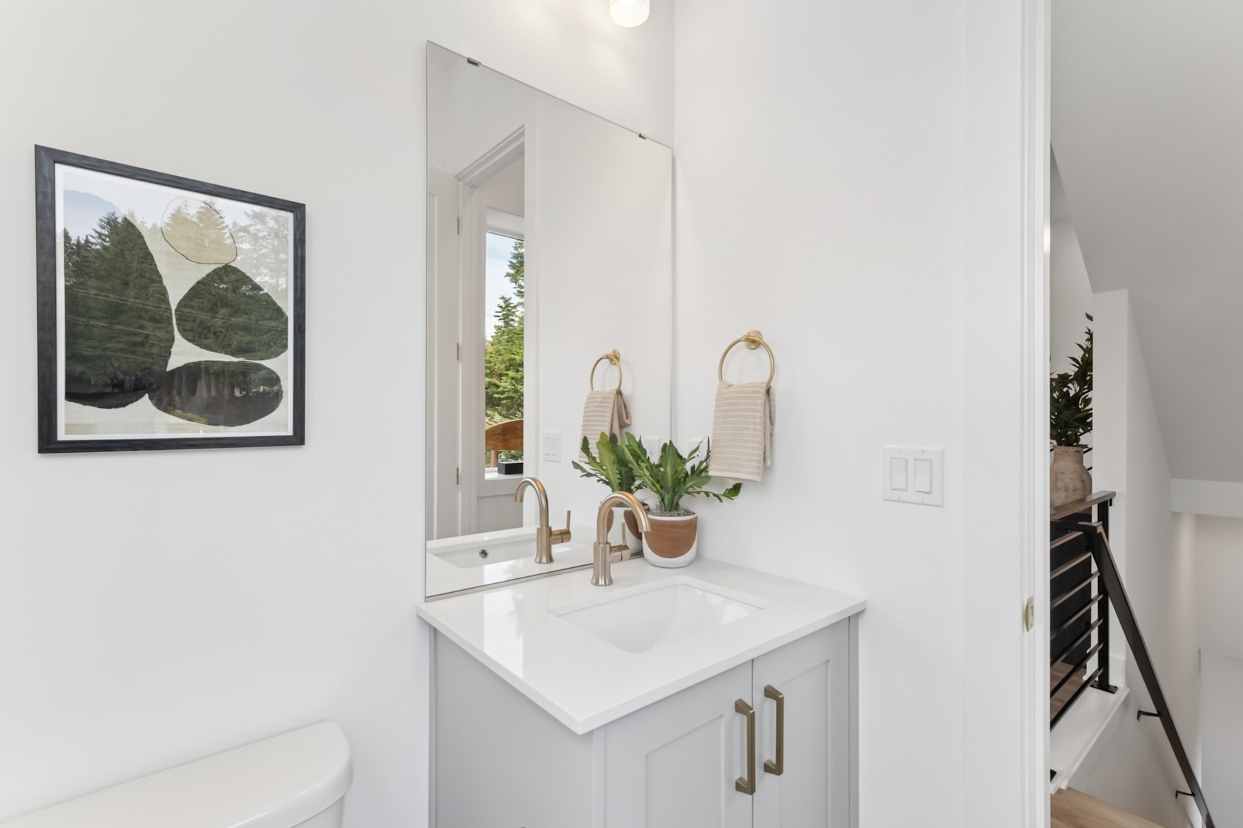 A modern and minimalist bathroom with a white vanity, a framed artwork on the wall, and a mirror with hanging decorative elements.