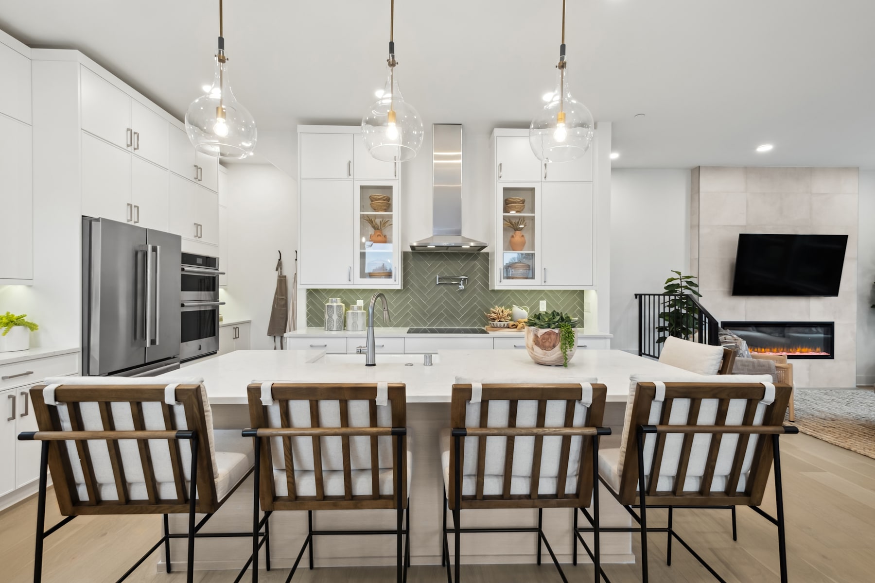 A modern, open-concept kitchen with a large island, pendant lighting, and a cozy seating area with a fireplace in the background.