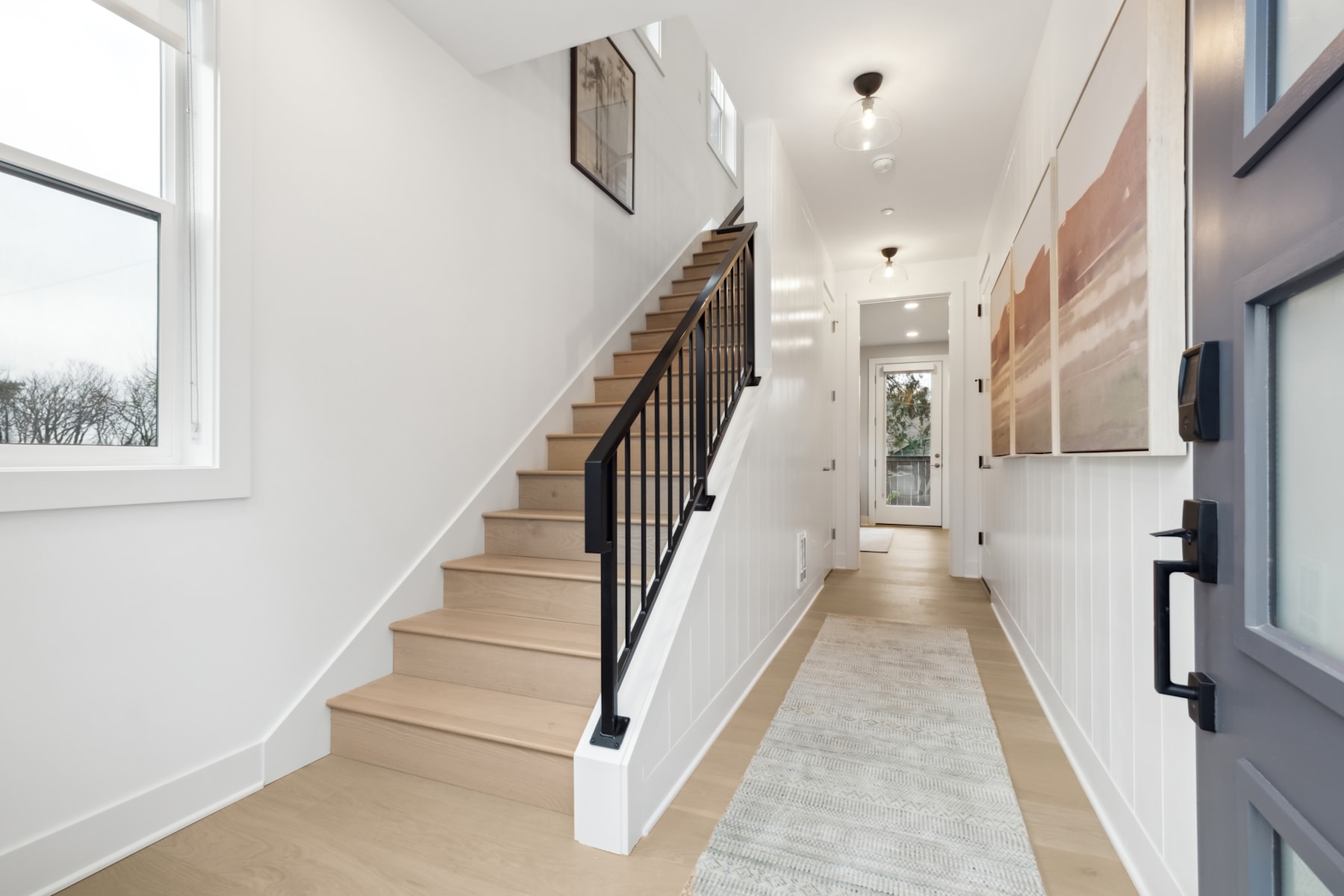 A bright and airy hallway with a wooden staircase leading up, surrounded by white walls and a tiled floor, with a window providing natural light.