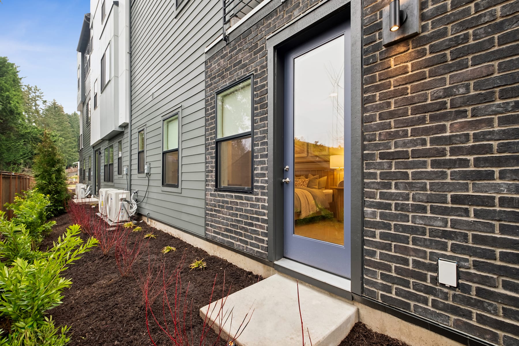 A modern, two-story residential building with a brick exterior, surrounded by a well-maintained garden and landscaping in the foreground.