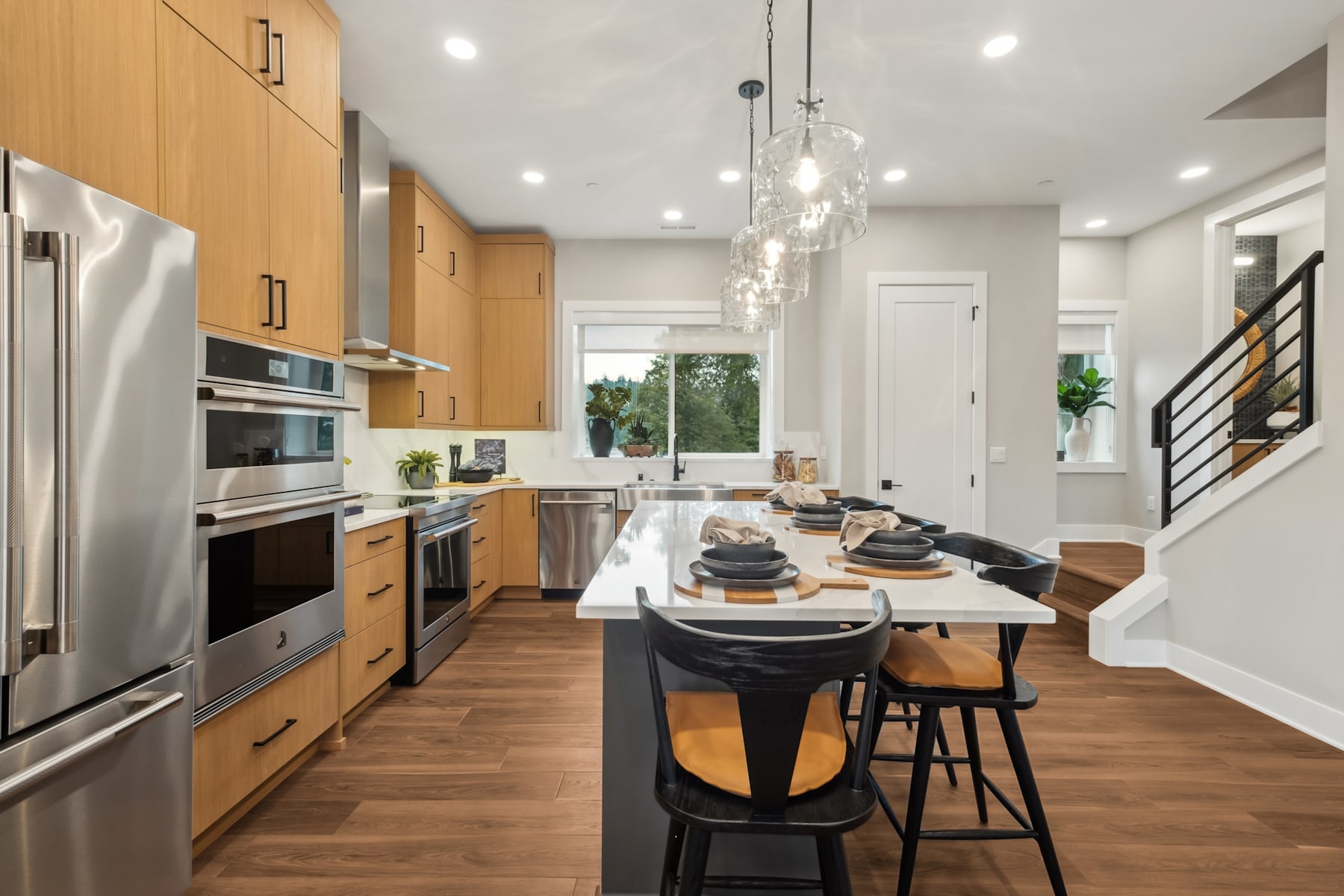 A modern and spacious kitchen with wooden cabinets, stainless steel appliances, a large island with a marble countertop, and pendant lighting fixtures creating a warm and inviting atmosphere.