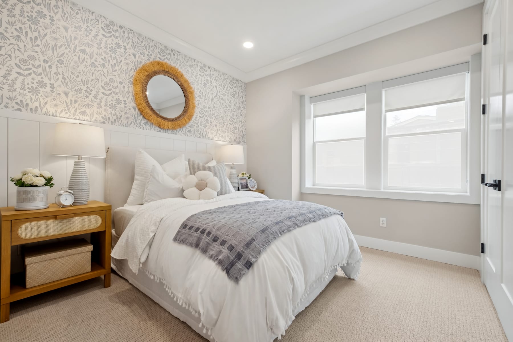 A cozy and inviting bedroom with a plush white bedding, a wooden nightstand, and a decorative mirror on the wall, set against a light-colored wallpaper pattern.