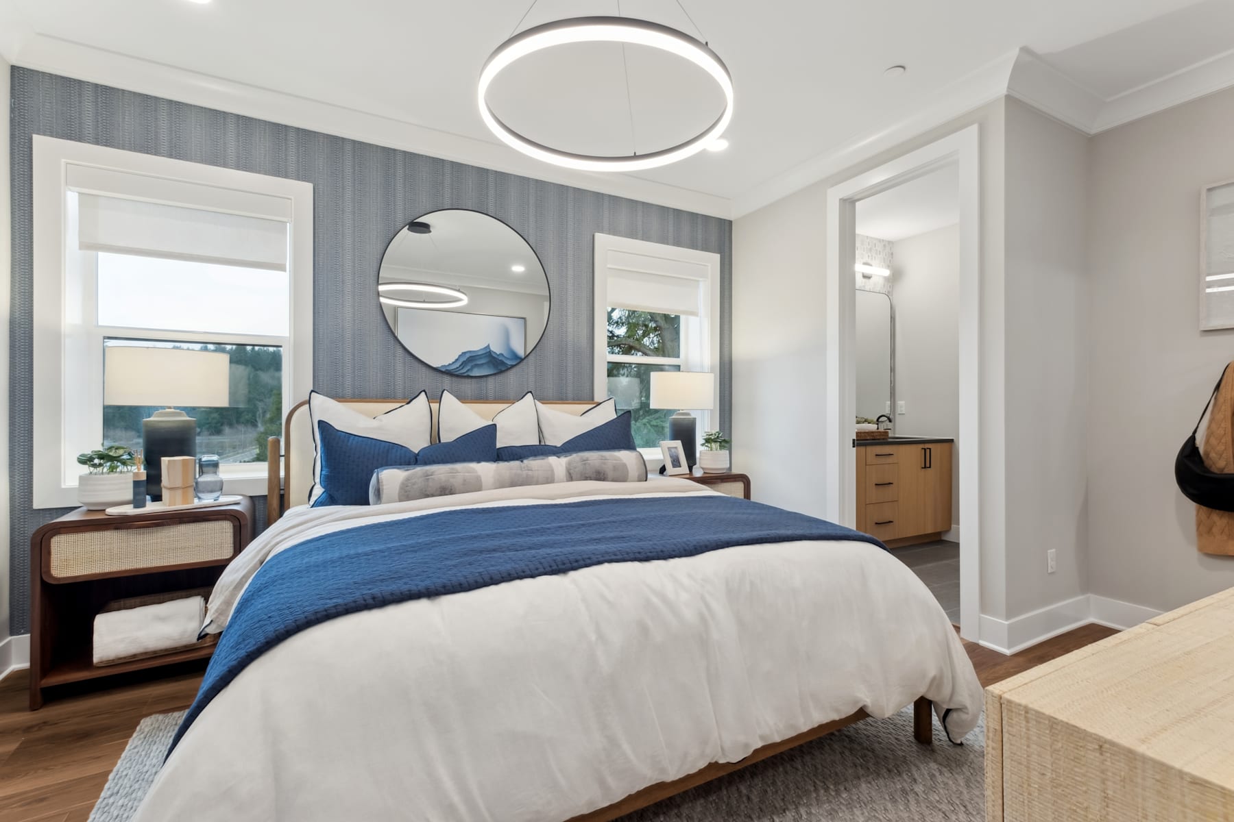 A modern and stylish bedroom with a large circular light fixture, a plush bed with blue and white bedding, and a round mirror on the wall.