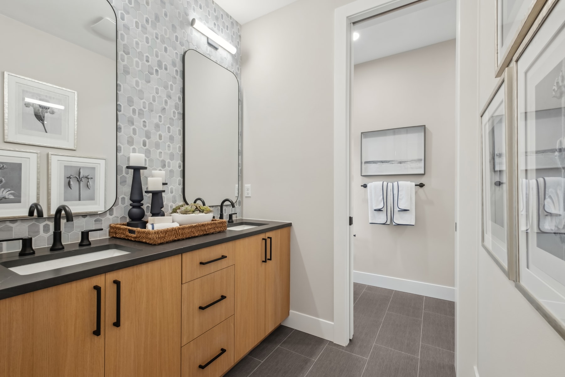 A modern and minimalist bathroom with a wooden vanity, a tiled backsplash, and framed artwork on the walls.