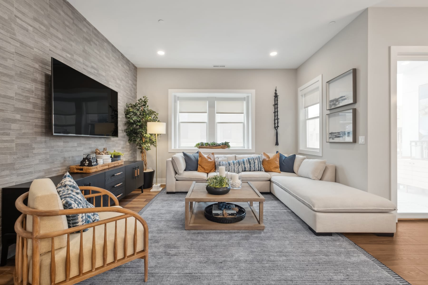 A cozy and well-designed living room with a large sectional sofa, a wooden coffee table, and a mounted TV on the wall, surrounded by decorative elements and natural lighting from the windows.