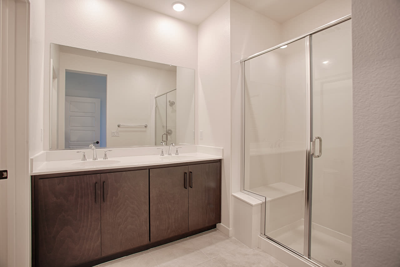 A modern bathroom with a double vanity, a glass-enclosed shower, and a neutral color scheme.