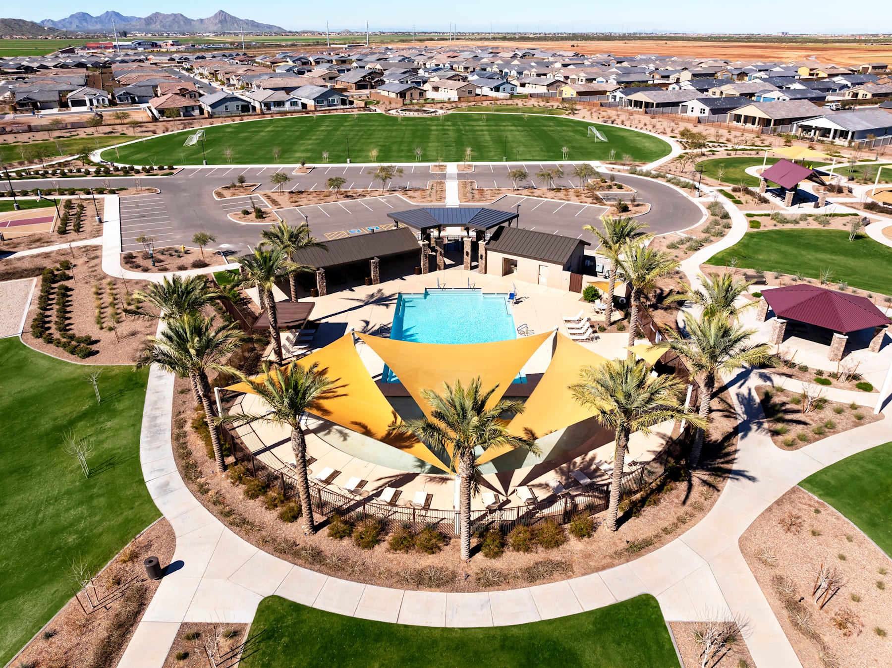 A sprawling residential community with a central pool and recreational area, surrounded by lush greenery and towering mountains in the distance.