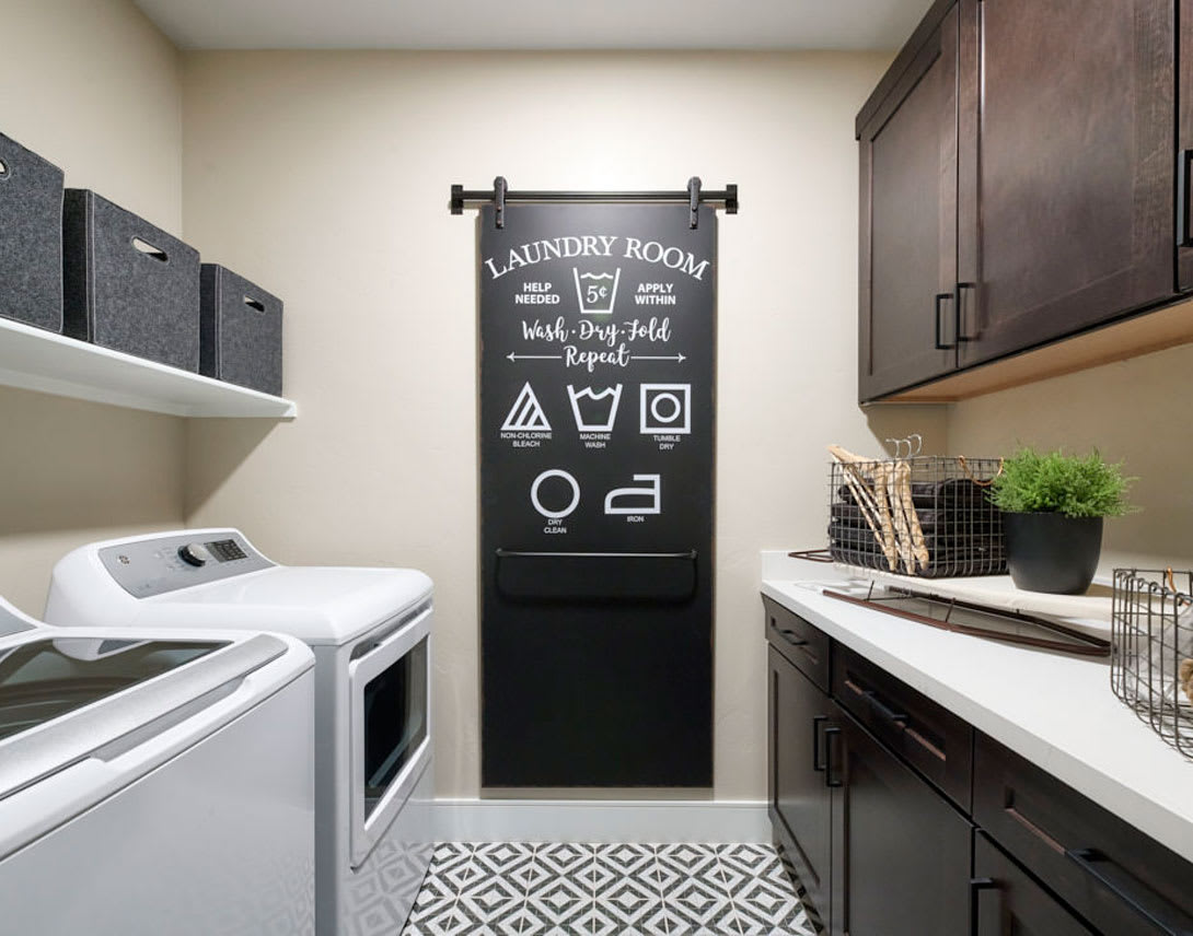 A modern and organized laundry room with a chalkboard sign, a washing machine, and various storage cabinets and shelves.