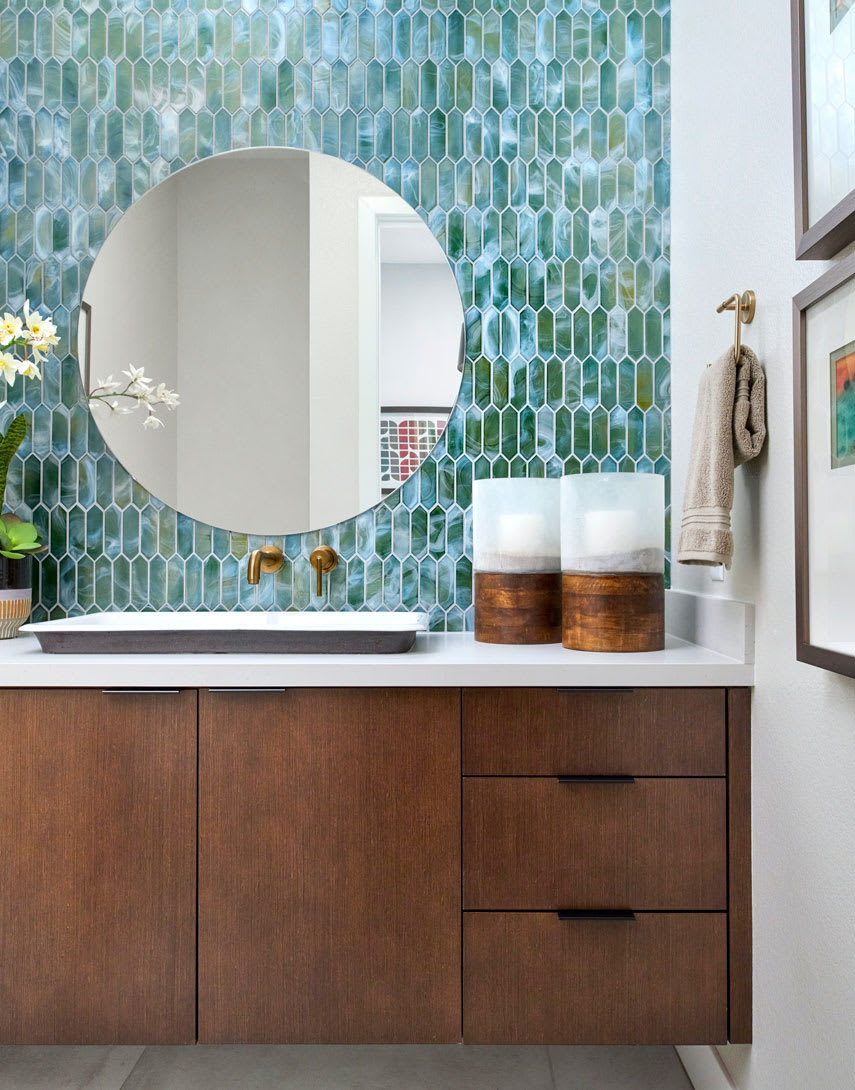 A modern bathroom vanity with a round mirror, wooden cabinets, and a vibrant green hexagonal tile backsplash.