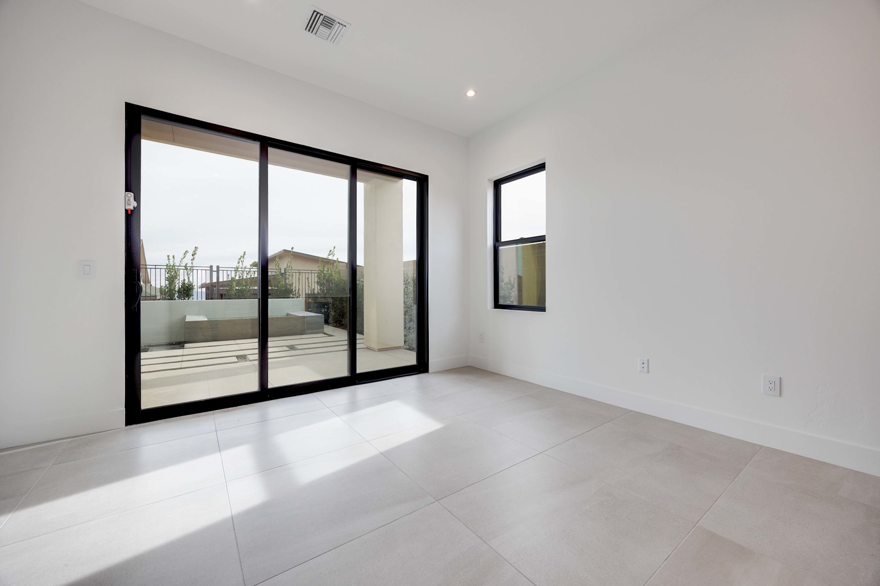 A bright, minimalist interior space with large sliding glass doors leading to an outdoor area, featuring clean lines, neutral colors, and a sense of openness and natural light.