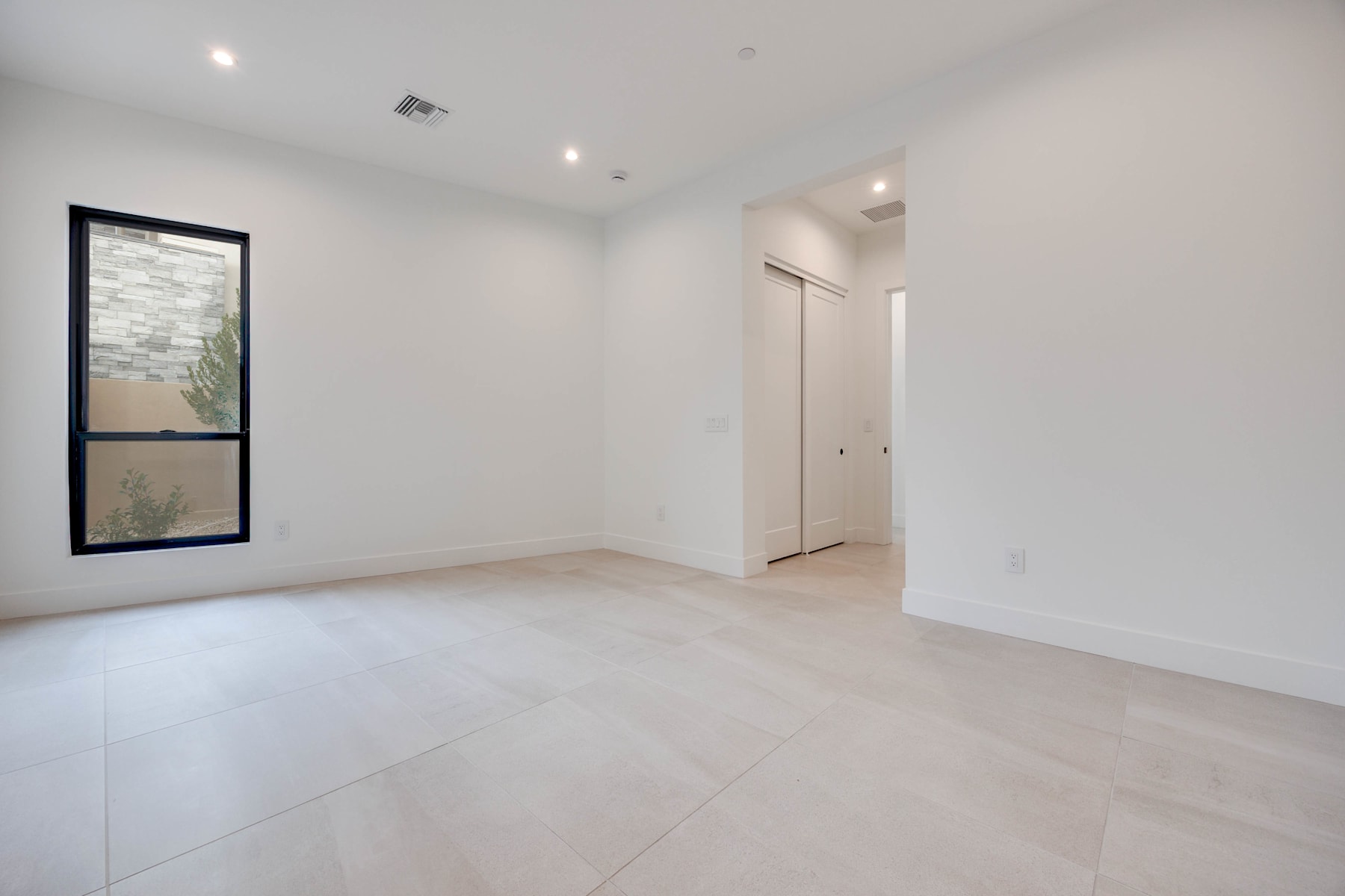 A minimalist, well-lit room with white walls, a large window, and a hardwood floor.