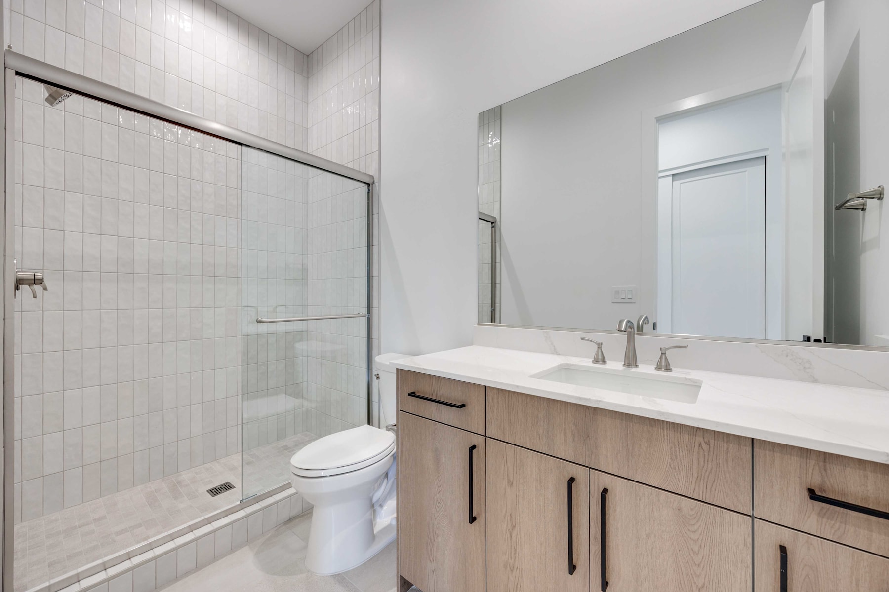 A modern bathroom with a vanity, toilet, and glass-enclosed shower, featuring a clean and minimalist design.