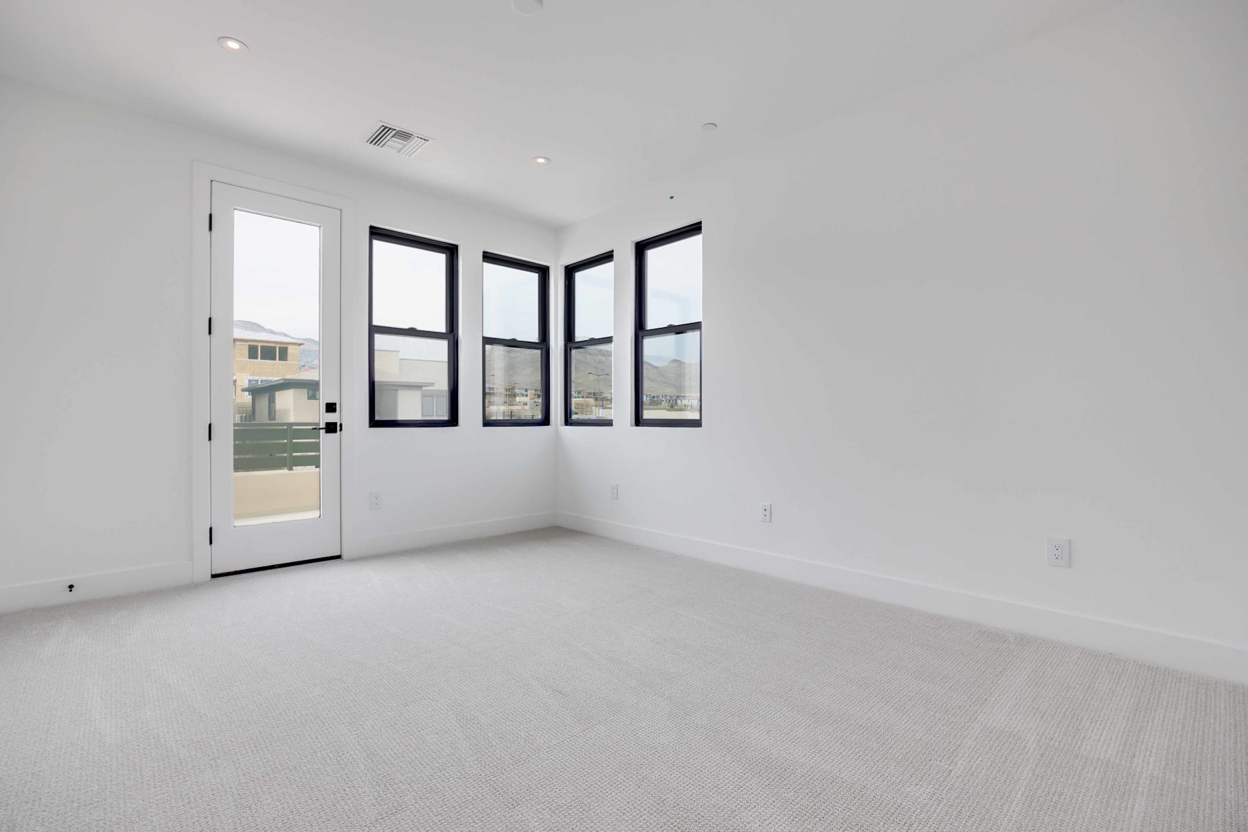 A bright, minimalist room with large windows, a white floor, and a door leading to the exterior.