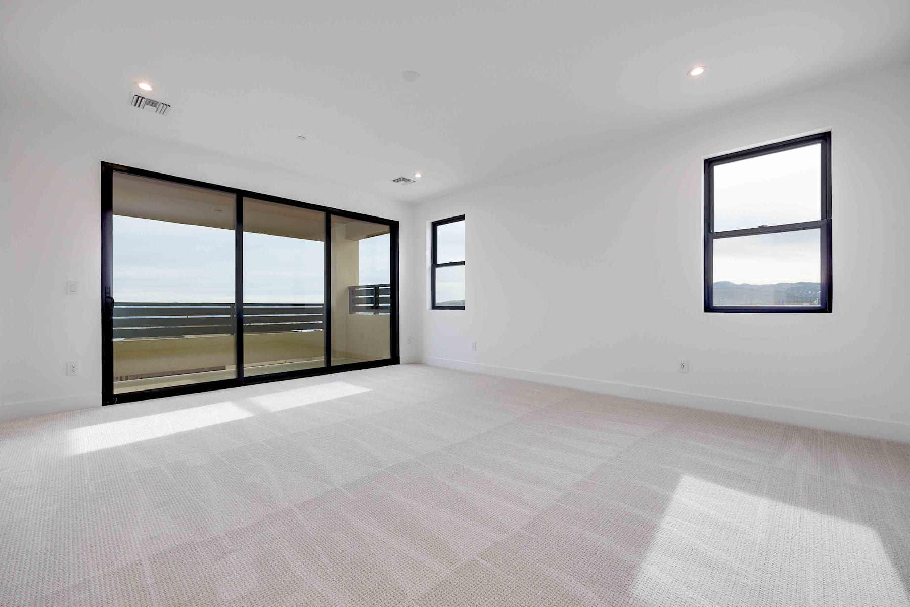 A spacious, minimalist room with large windows offering a scenic view of the outdoors, featuring a clean, white interior and sleek, black-framed windows.