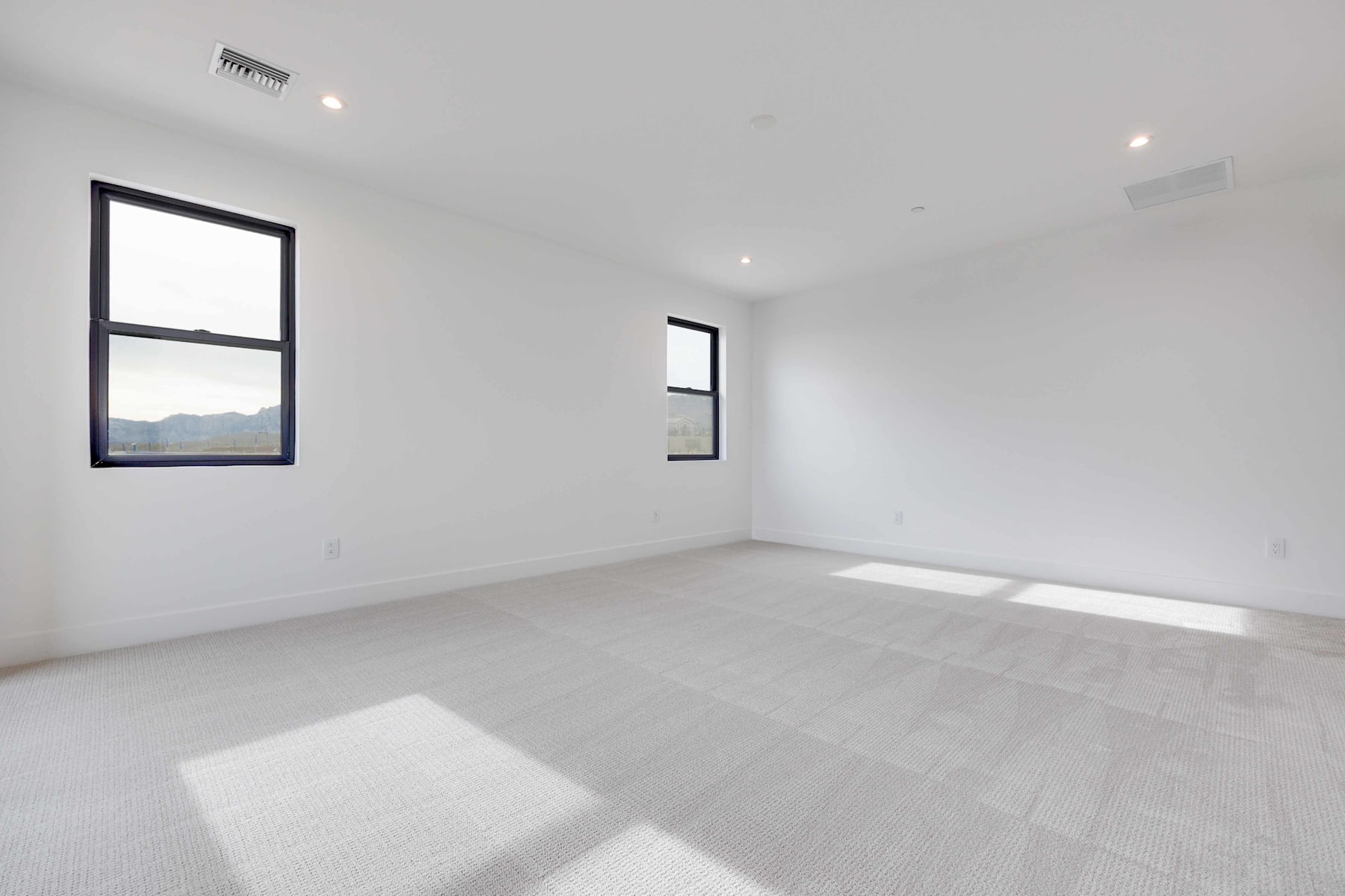 A spacious, minimalist room with large windows offering a view of the outdoors, featuring a clean, white interior and a hardwood floor.