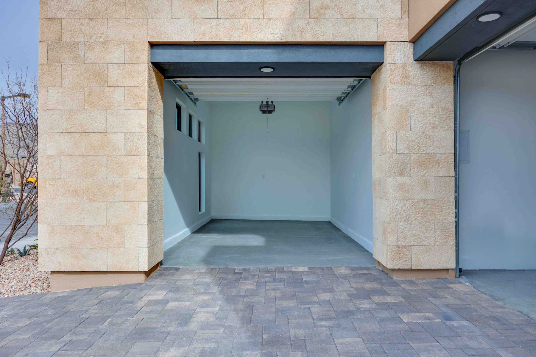 A covered entryway with a tiled floor leading to a recessed doorway, surrounded by a stone facade and a modern architectural design.