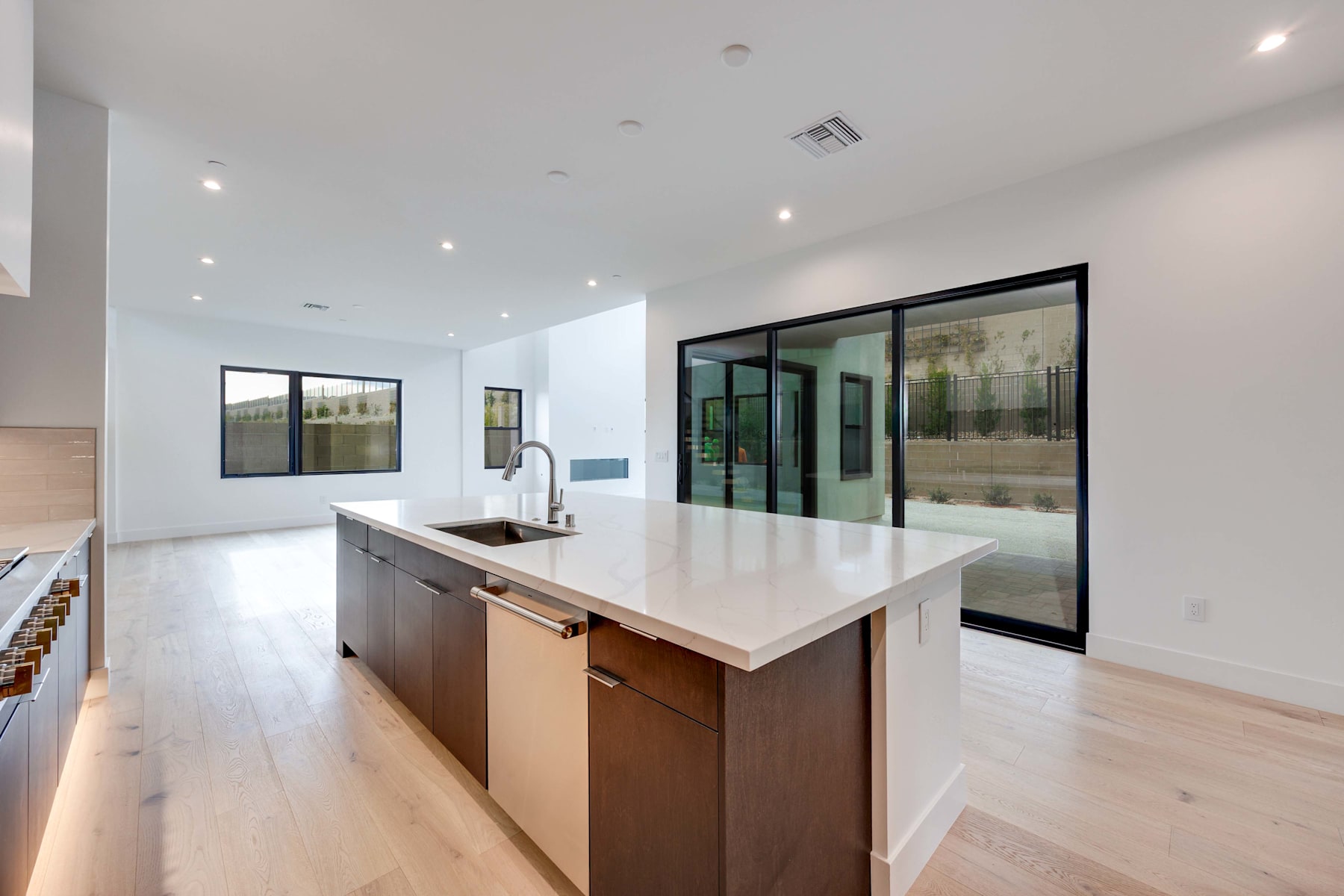A modern, open-concept kitchen with a large island countertop, wooden cabinets, and floor-to-ceiling windows providing ample natural light.
