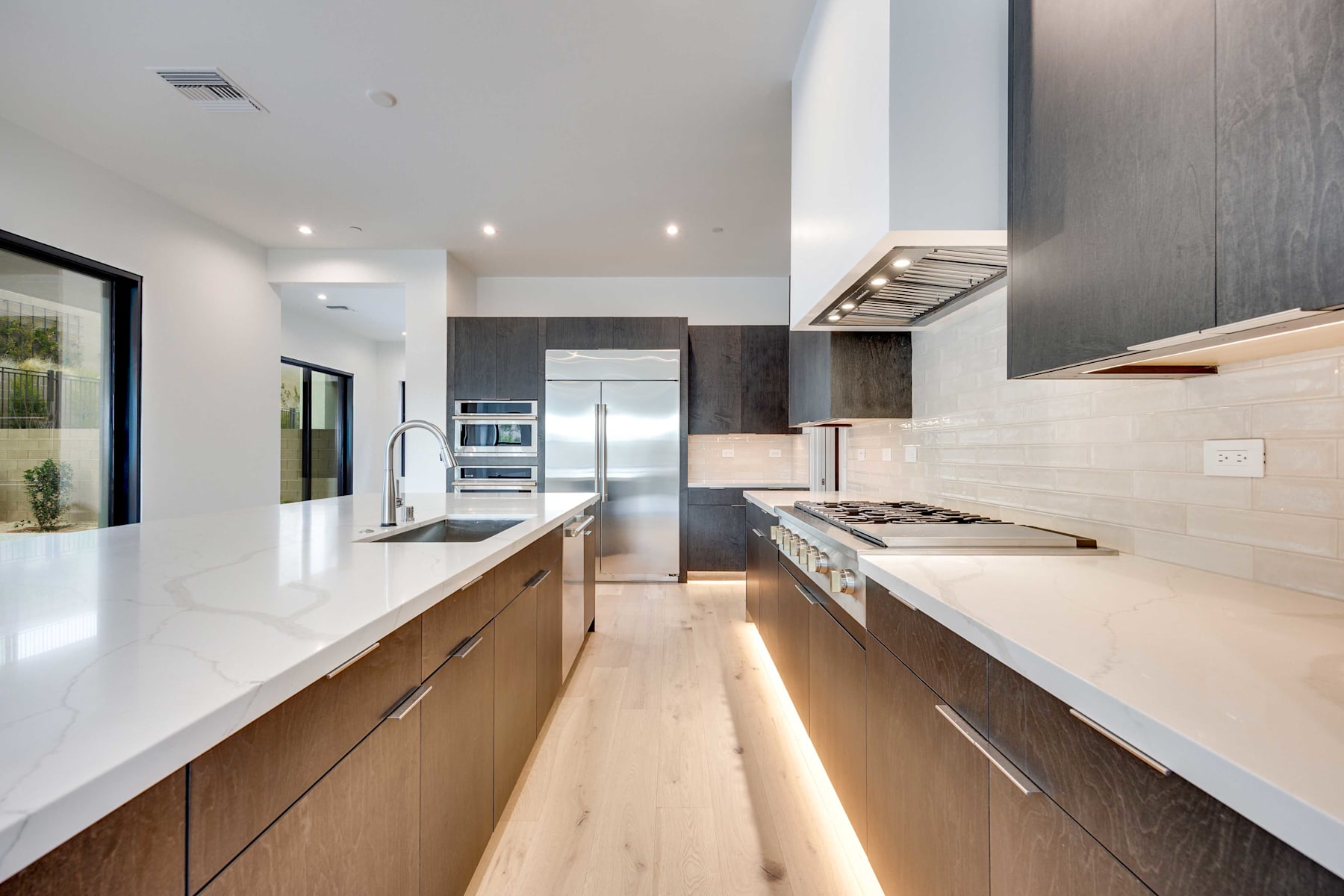 A modern, open-concept kitchen with sleek, wooden cabinetry, white countertops, and stainless steel appliances, leading into a bright and airy living space.