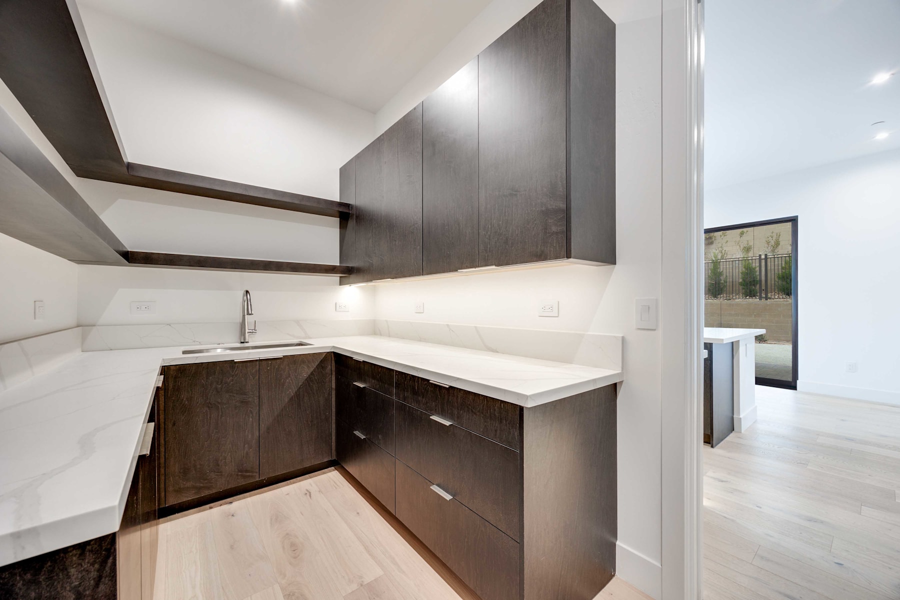 A modern, minimalist kitchen with dark wood cabinets, white countertops, and a sleek, open design.