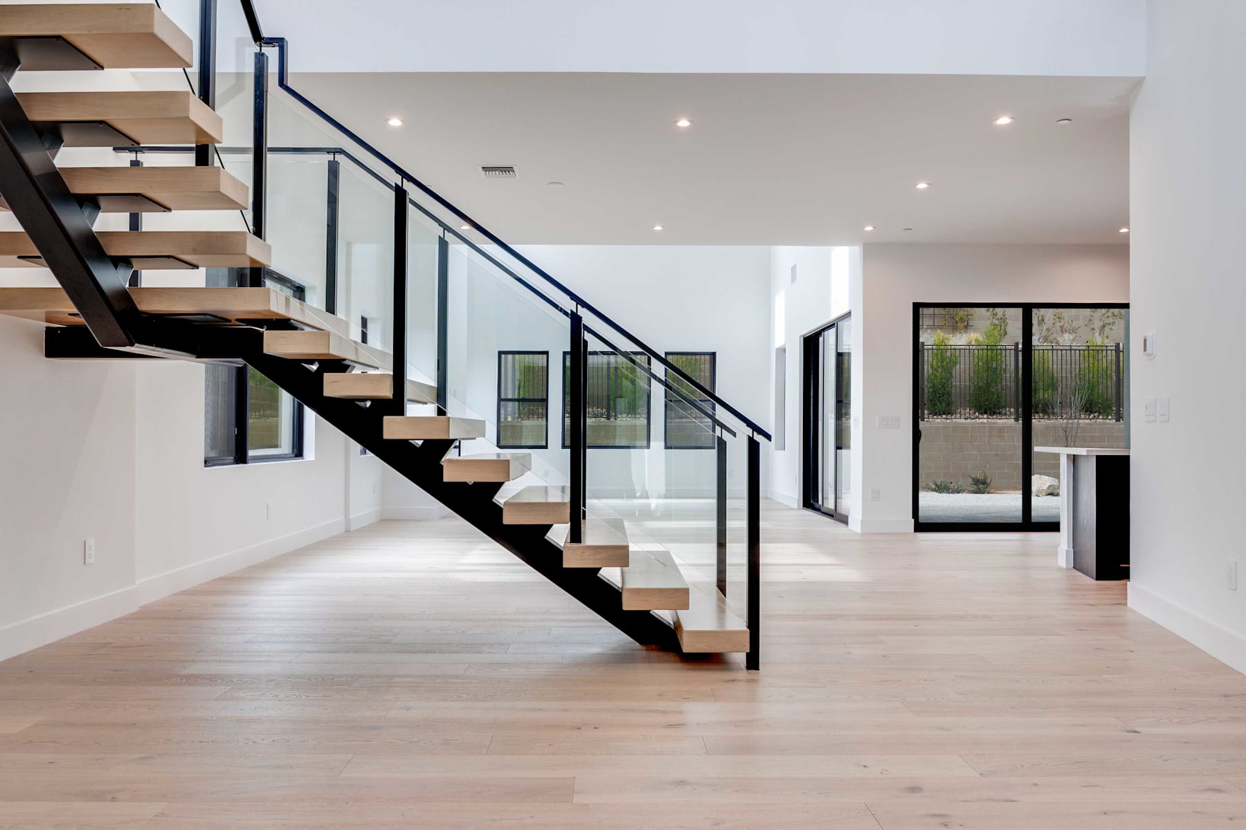 A modern, open-concept interior with a sleek, black metal staircase leading up to a second level, surrounded by large windows that allow natural light to flood the space.