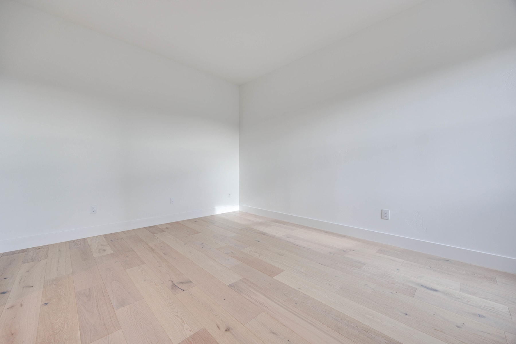 An empty room with white walls and a wooden floor, creating a clean and minimalist atmosphere.