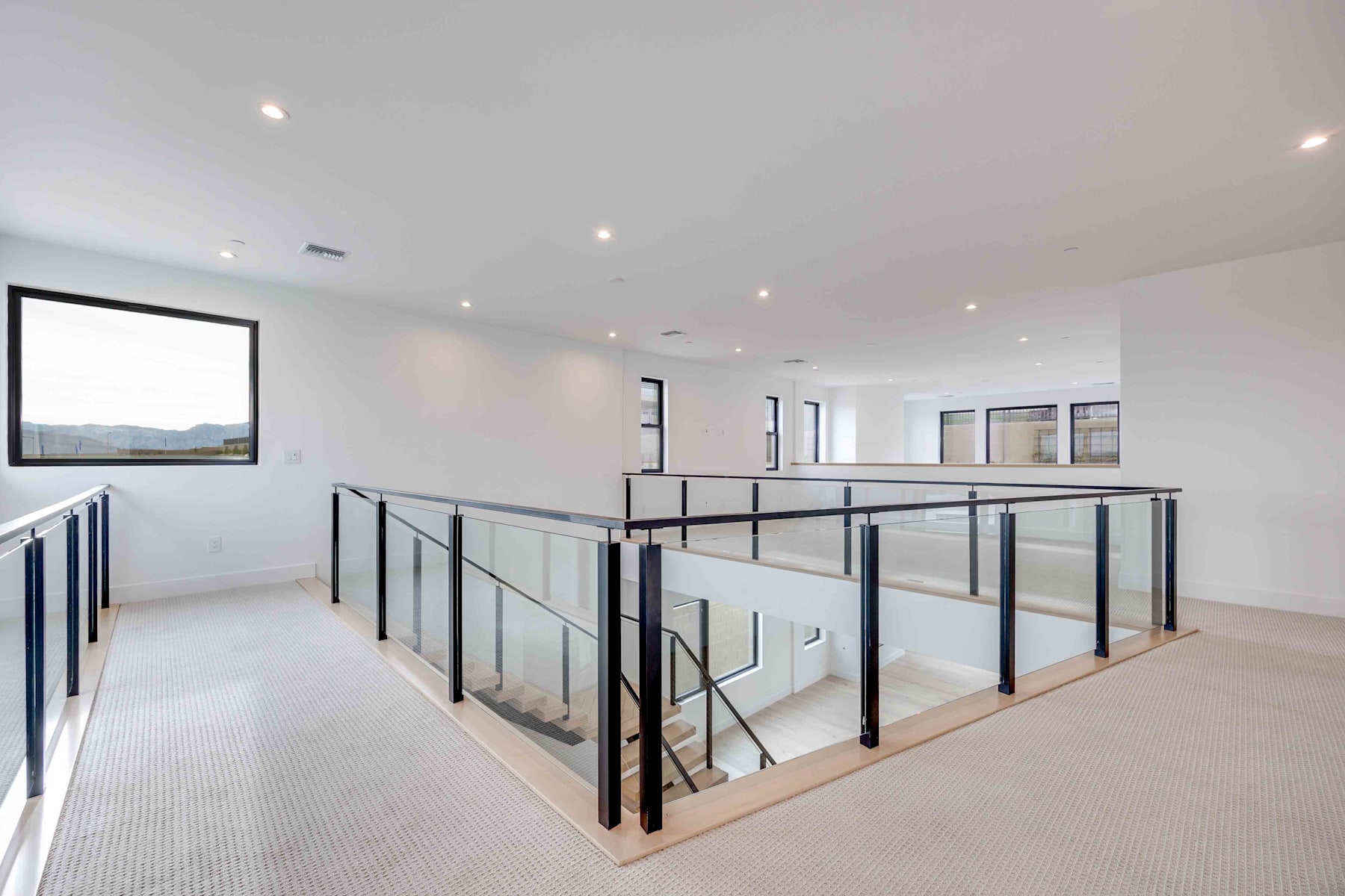 A modern, open-concept interior with a raised platform area surrounded by metal railings, against a backdrop of large windows overlooking a scenic landscape.